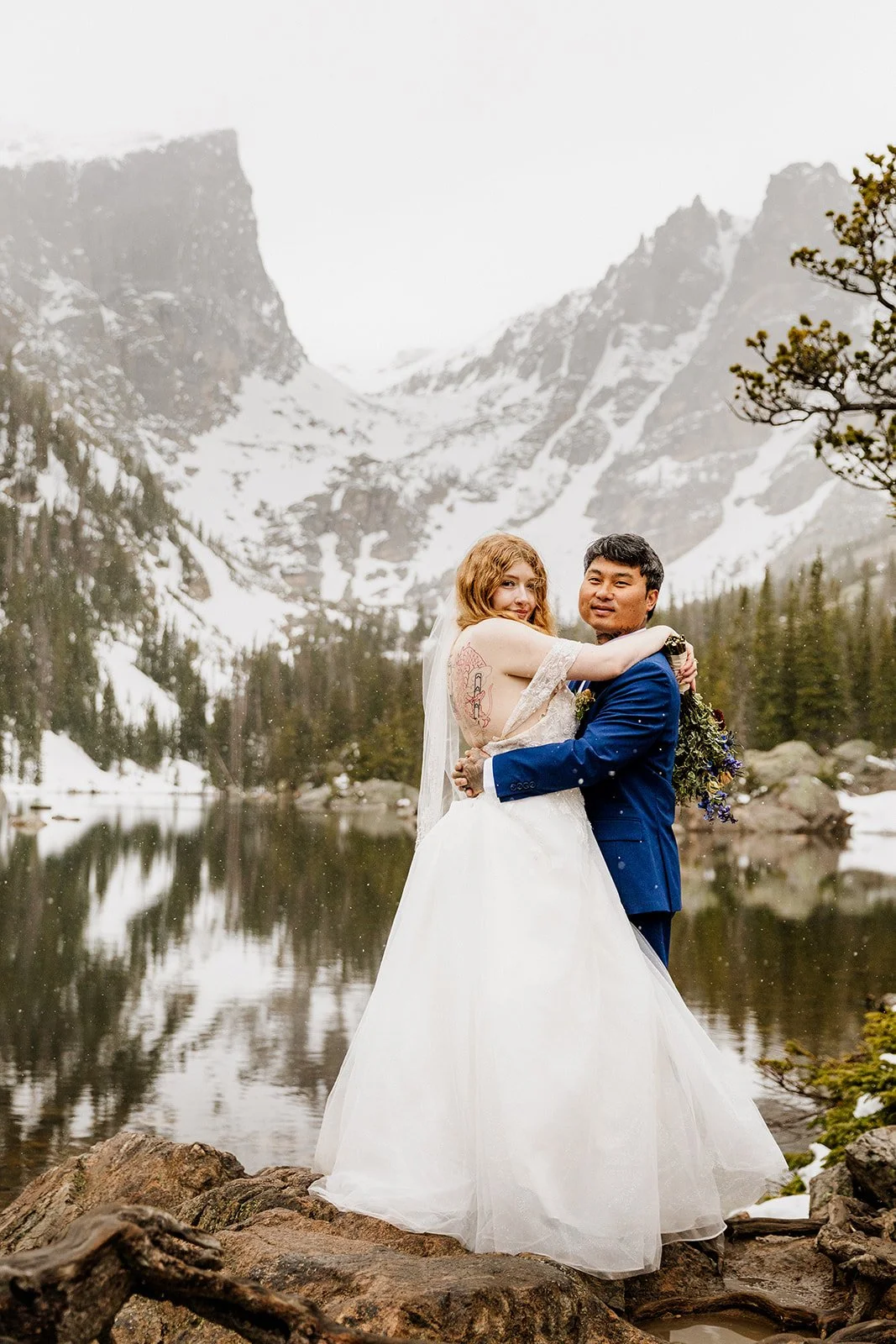 Couple hugging at Dream Lake with snow covered peaks behind them