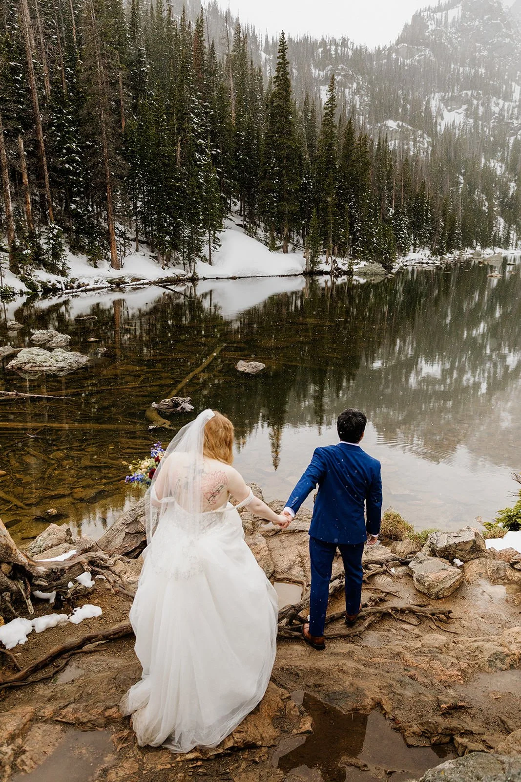 Groom leading the bride by the hand along the rocky shore of Dream Lake