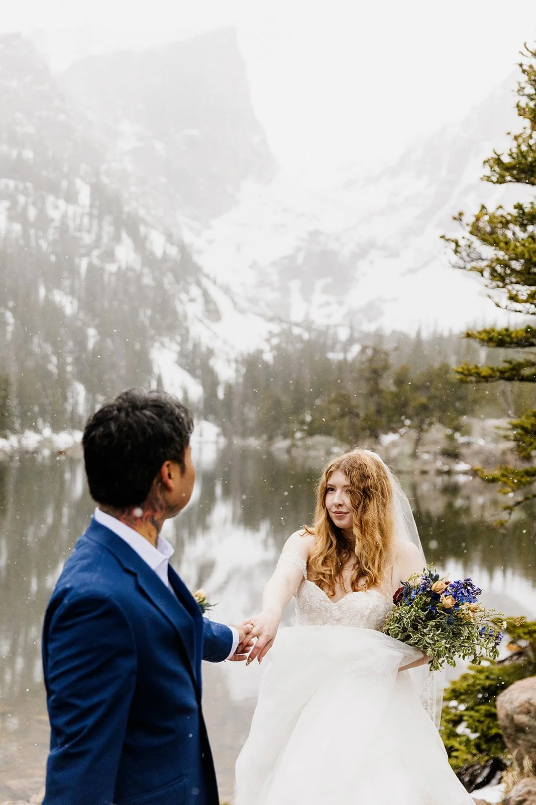 Groom looking back at the bride as they hold hands at the lake