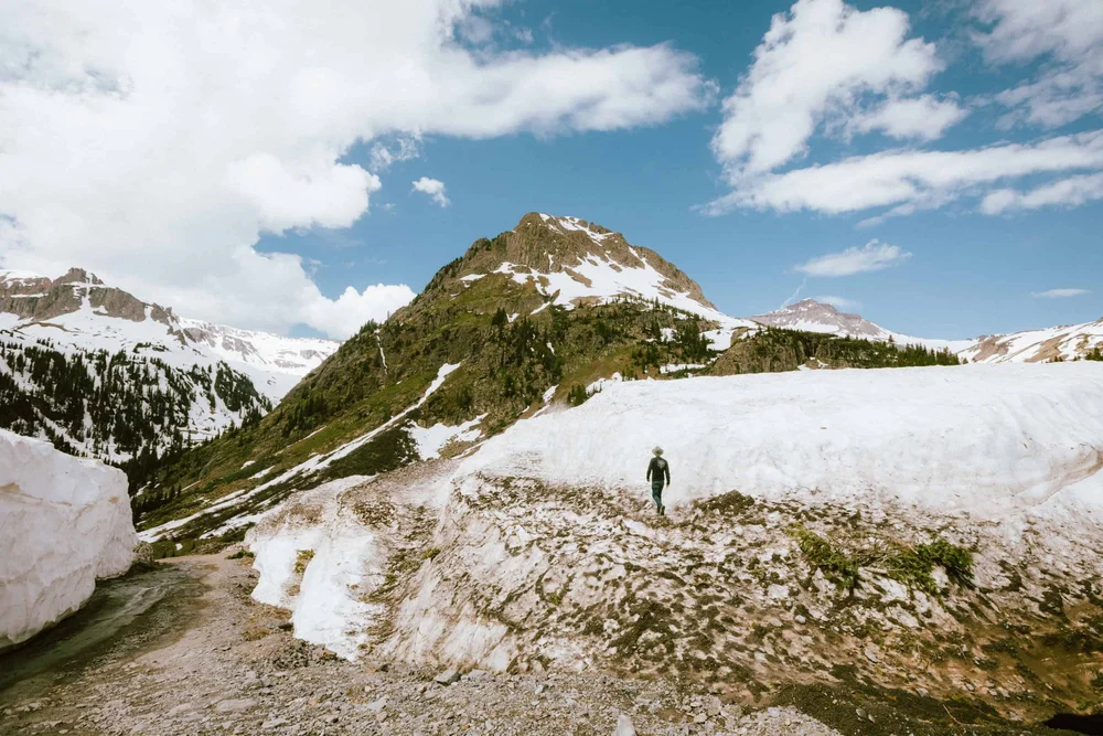 A person standing on a snowbank in Yankee Boy Basin near Ouray, Colorado, under a green peak