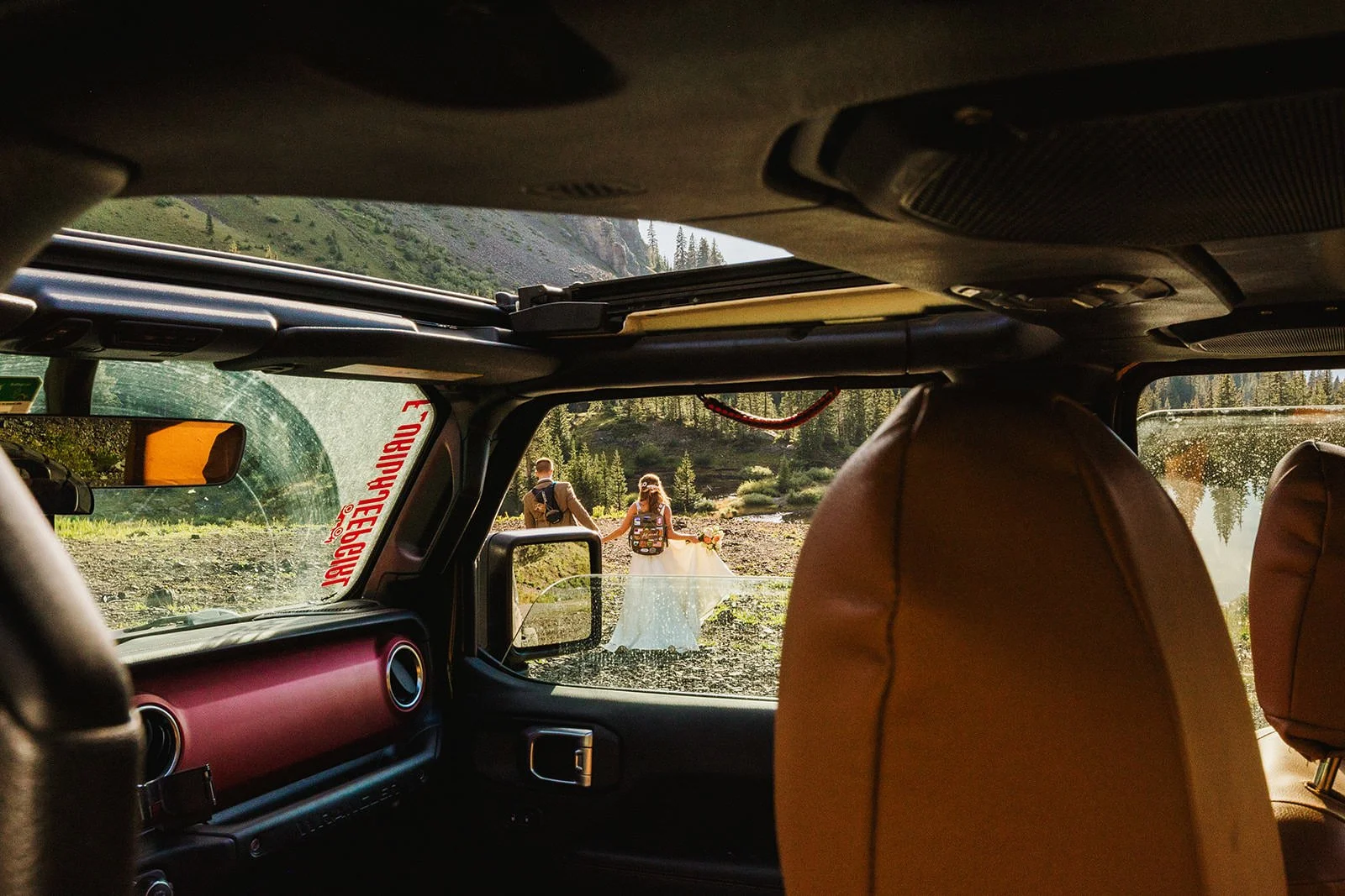 A photograph of a newly married couple eloping in Telluride, Colorado. They are walking away from the camera through the open window of a jeep, with majestic mountains rising in the distance.