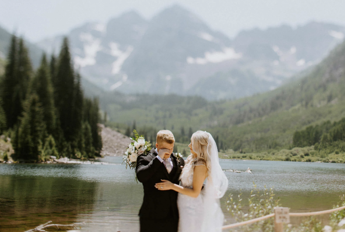Couple hugging beside an alpine lake surrounded by pine trees and snowy peaks near Aspen