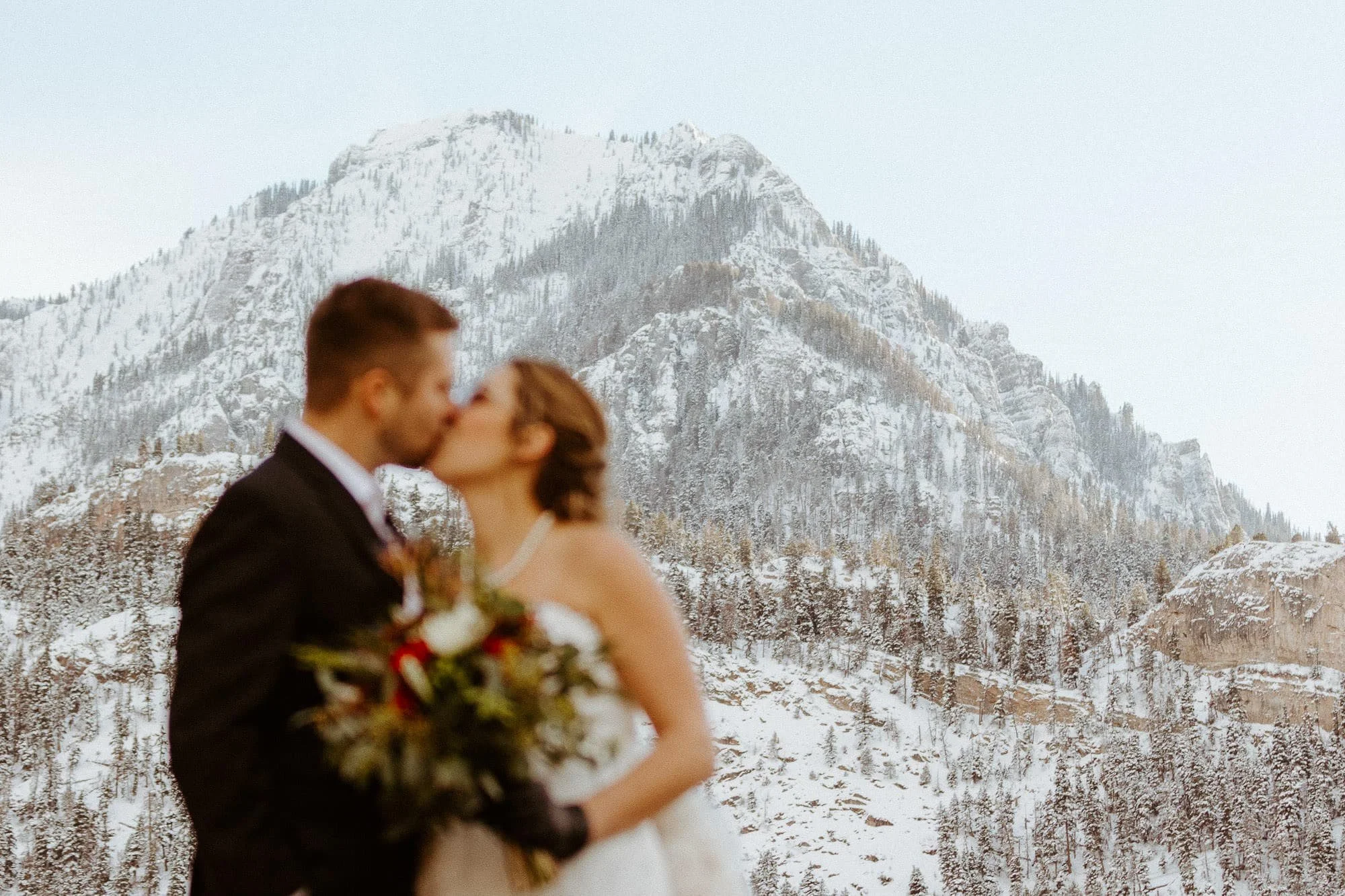 A couple kiss in front of the mountains around Ouray while holding a bouquet in their wedding clothes