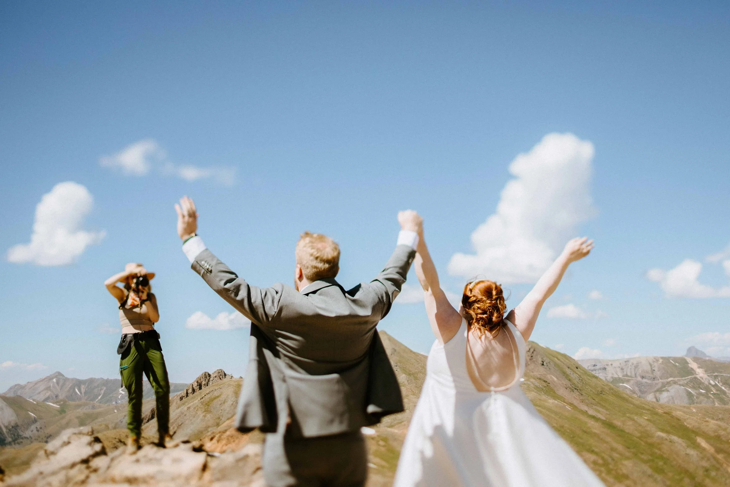 People celebrating outdoors on a mountain landscape with a clear blue sky, raising their hands and taking photos.