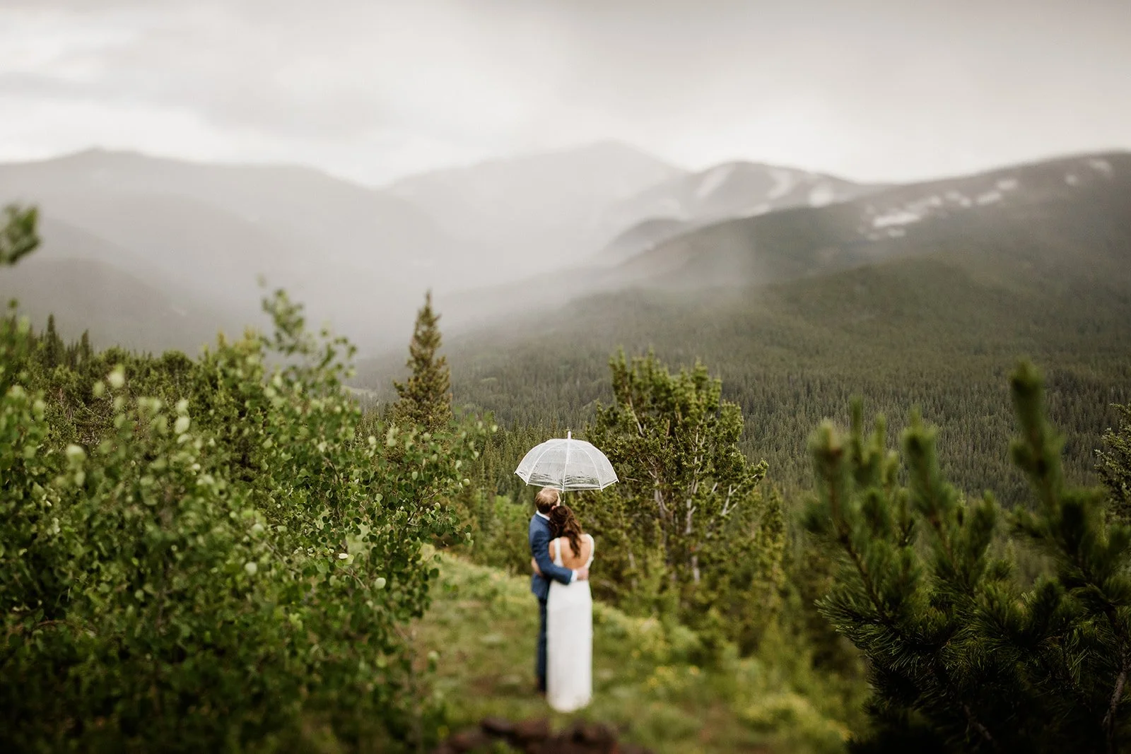 Couple sharing an umbrella on a forested mountain path during their Colorado elopement