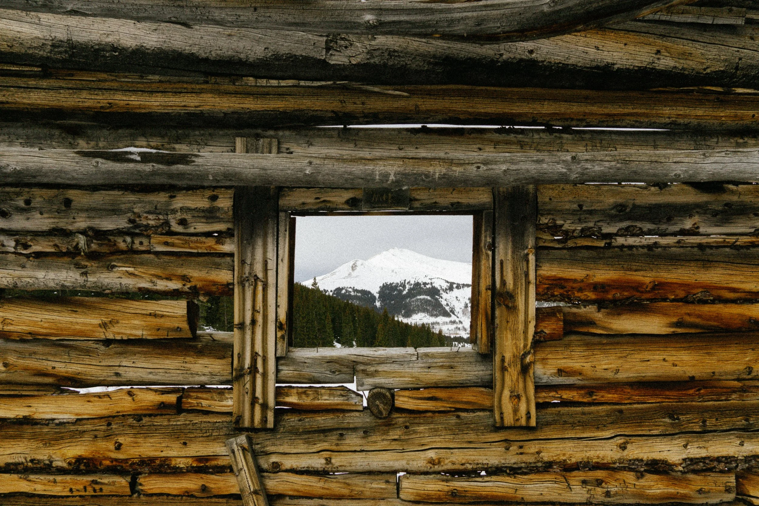 A snowy peak framed through the window of an old mining cabin at Mayflower Gulch