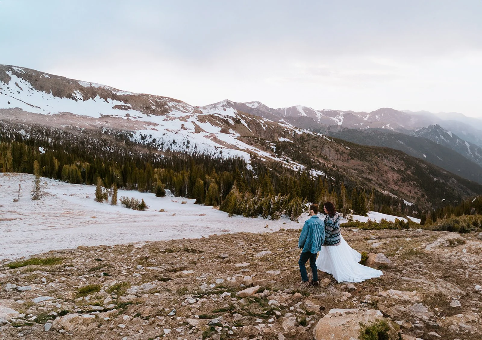 A couple wearing jackets holds hands while walk around rocky mountain national park