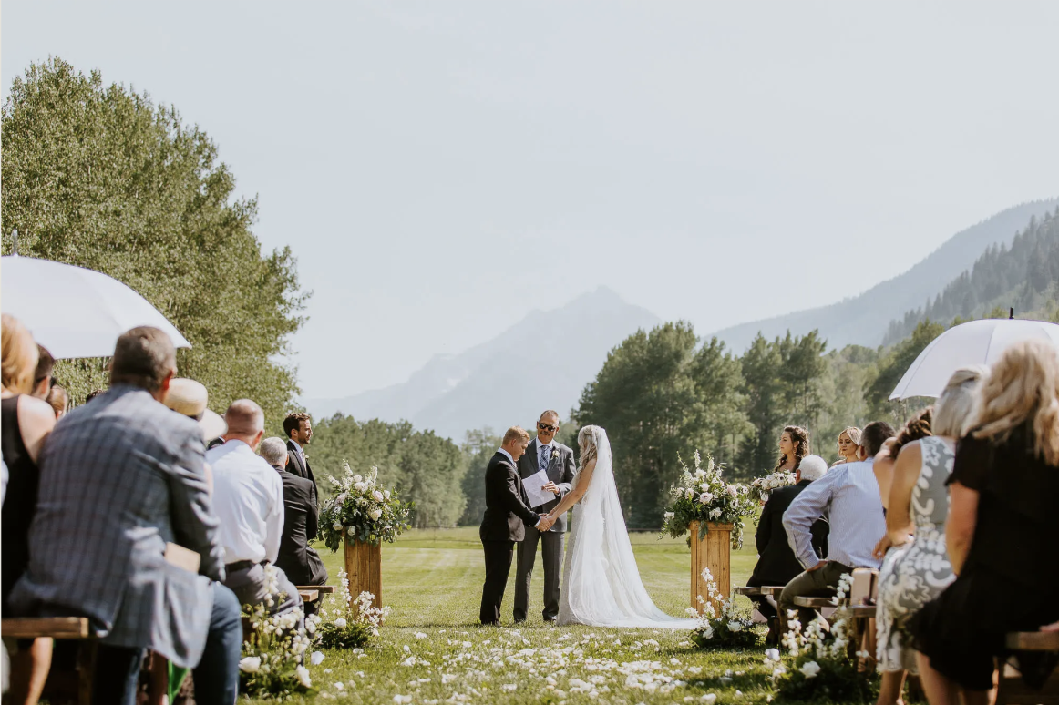 Outdoor wedding ceremony in a grassy mountain meadow in Aspen, Colorado with guests seated under cloudy skies