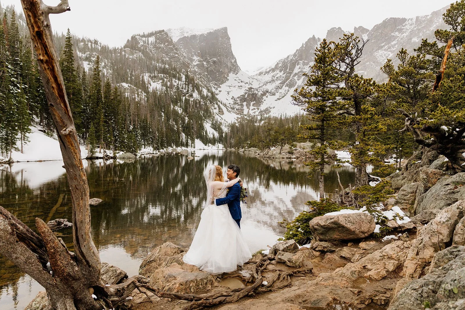 Couple hugging at Dream Lake with snow falling and Hallett Peak behind them
