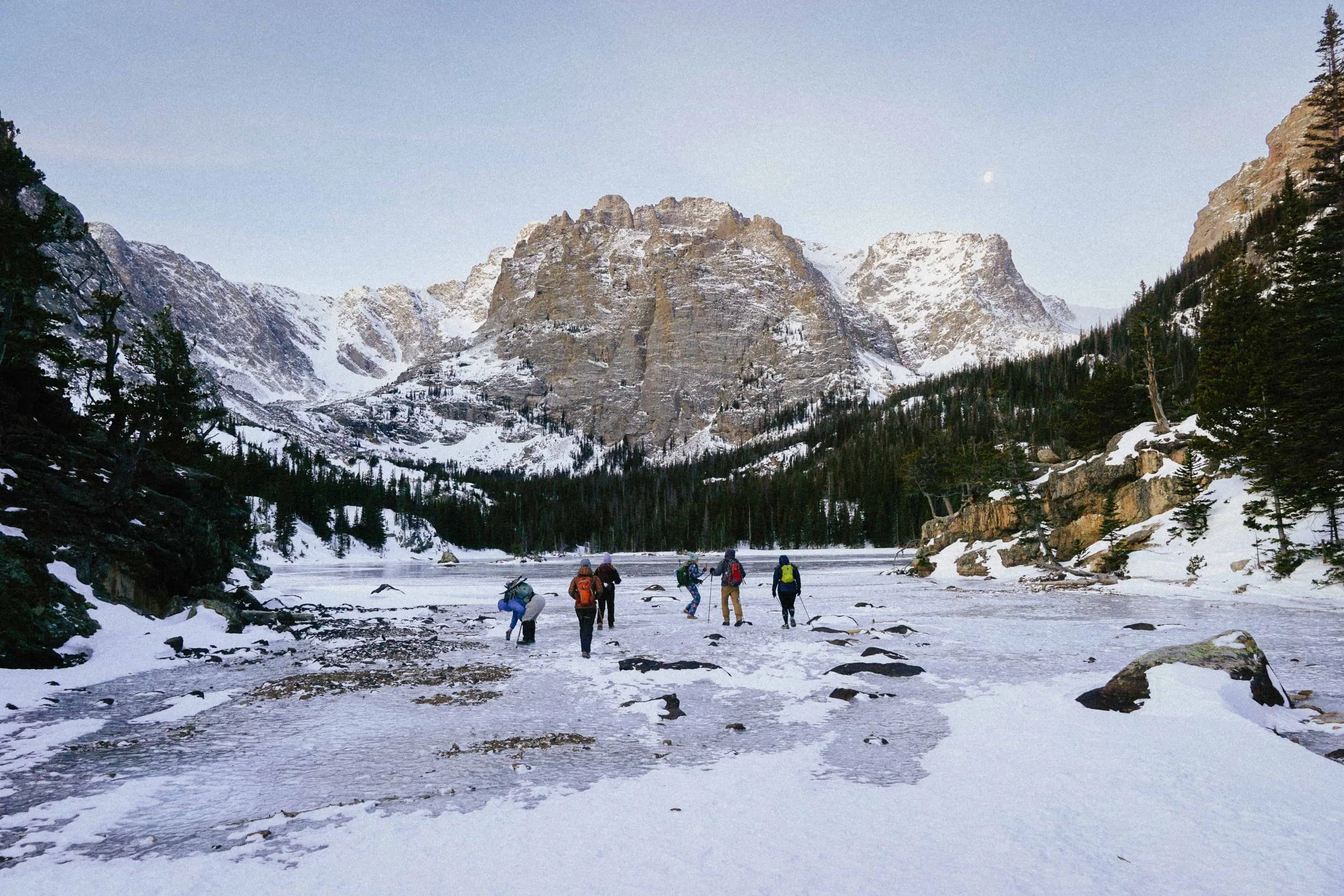 Hikers crossing the frozen Loch in winter below the peaks of Rocky Mountain National Park