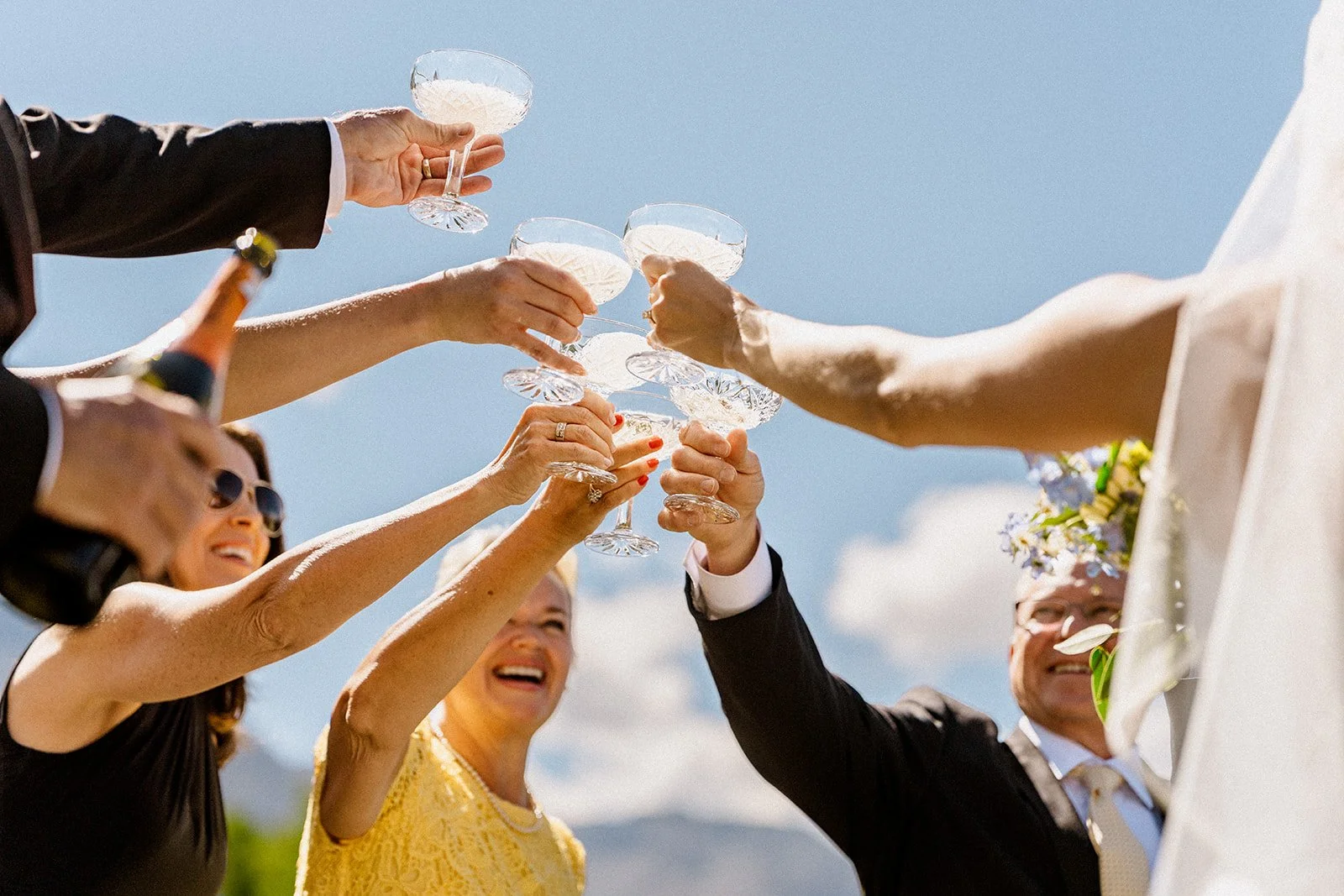 Family and loved ones cheers with champagne coupe glasses with a blue sky behind them and everyone smiling