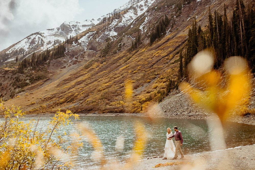 A couple surrounded by golden aspen leaves beside an alpine lake during a fall elopement in Crested Butte, Colorado