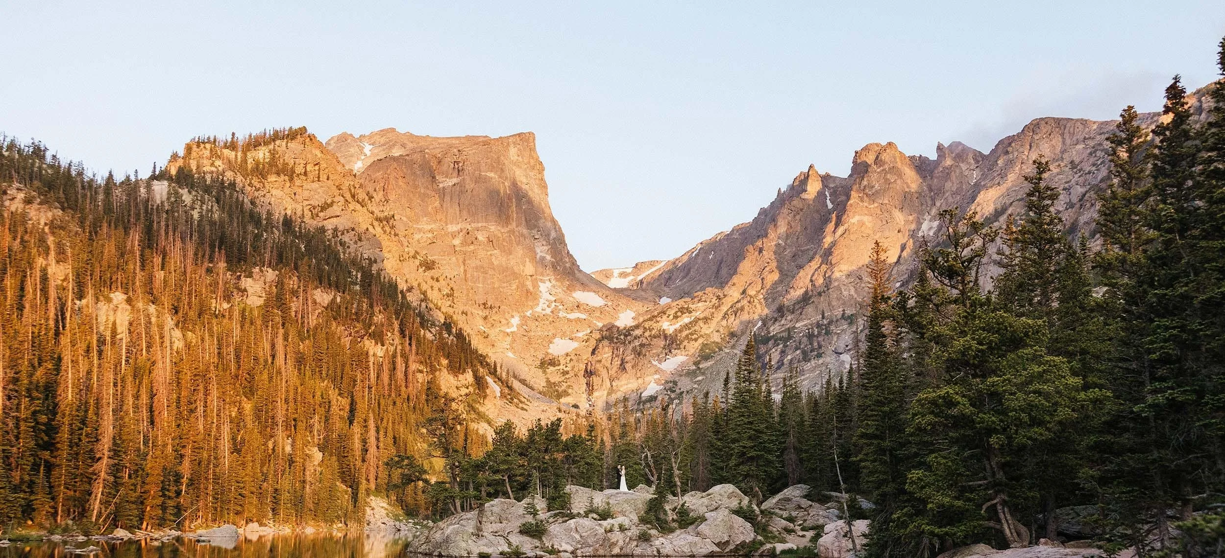 A couple in wedding attire stands in front of the mountains of Dream Lake