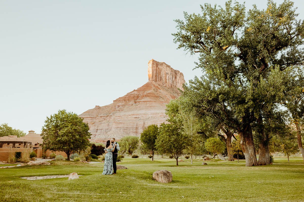 Couple on the lawn at Gateway Canyons Resort, with a tall red rock tower behind them