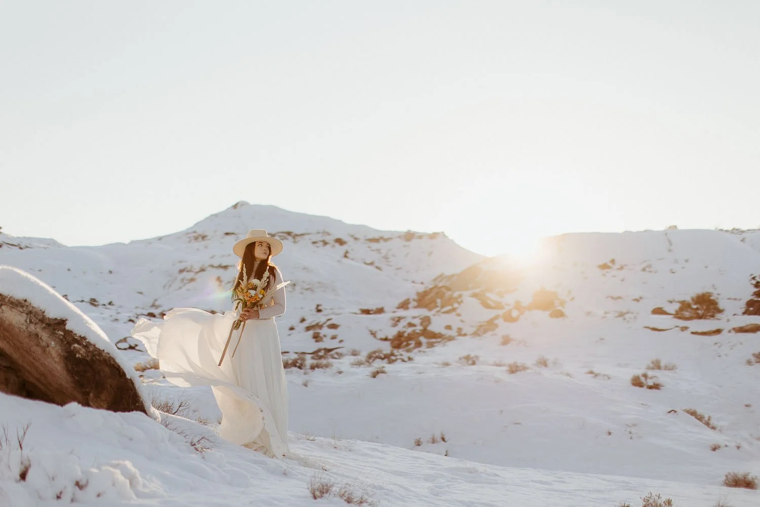 A bride holds her bouquet in the snow at sunset near Grand Junction