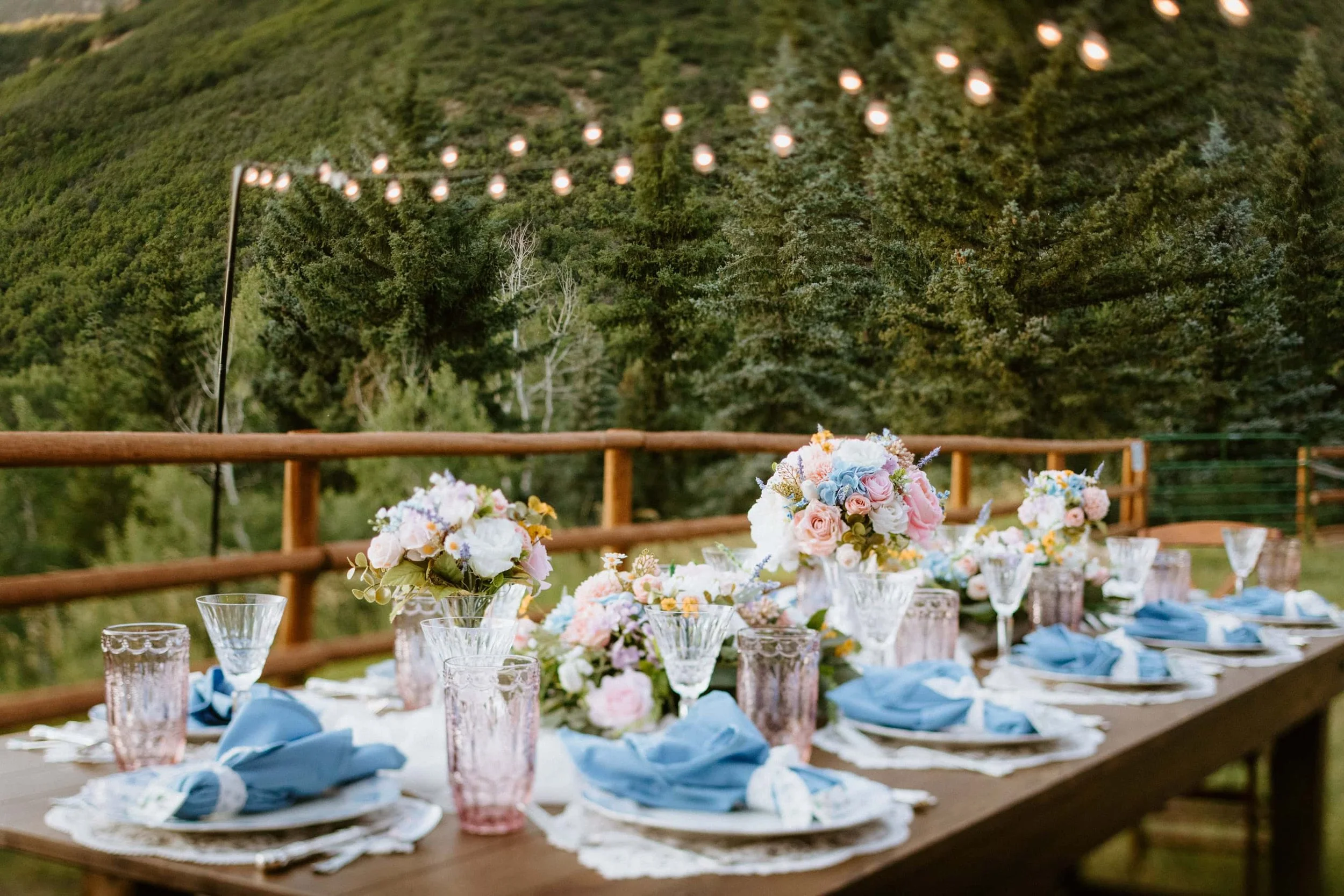 An outdoor dinner table under string lights set with flowers and blue napkins for a reception after eloping
