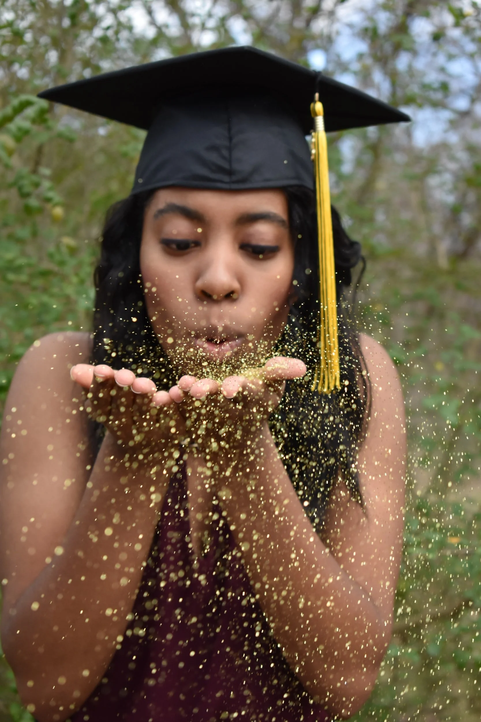 Graduate in a cap blows a handful of gold glitter
