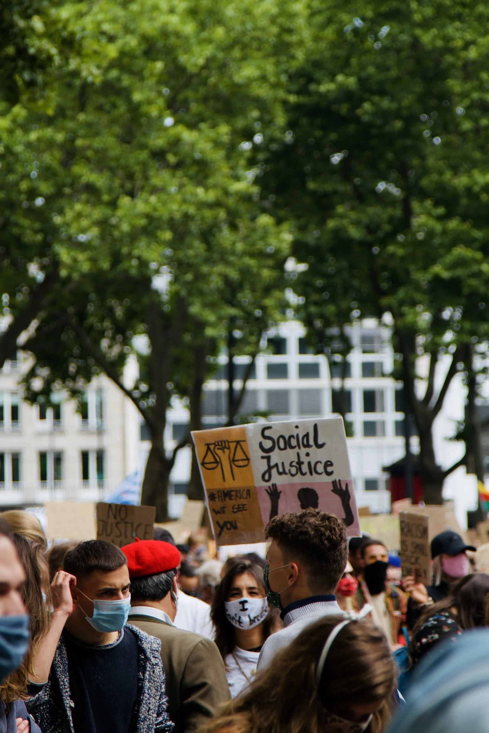 Protesters and a sign that reads "Social Justice #America we see you" with drawings of justice scales and a silhouette with their hands up