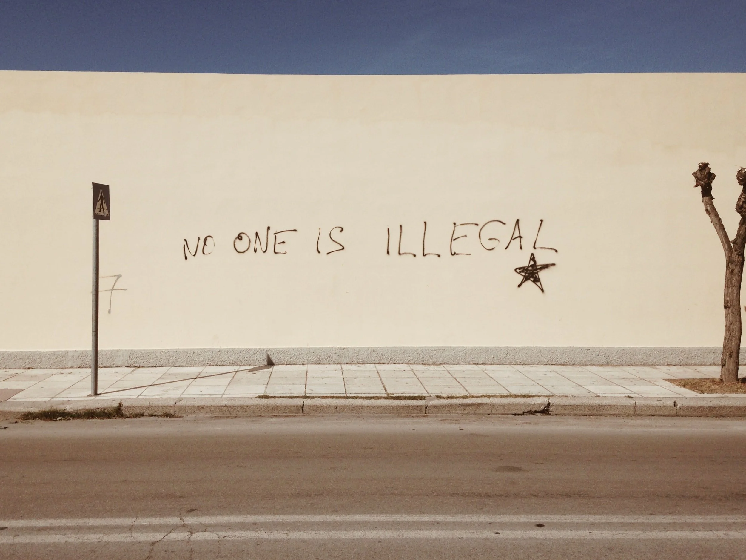 Black graffiti on a beige wall that reads "no one is illegal"