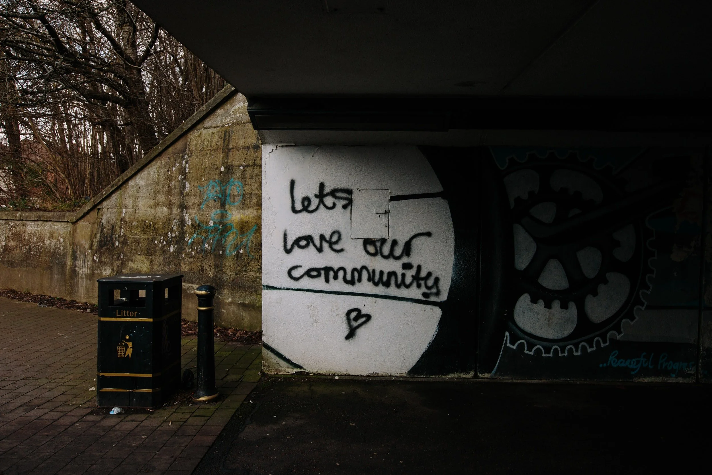 Black graffiti on a white wall that reads " let's love our community"