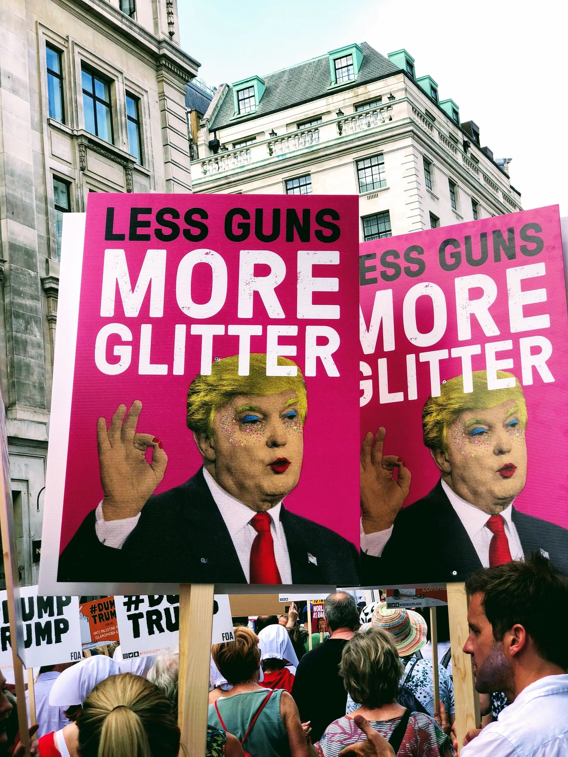 Protest sign that reads "less guns, more glitter" with a picture of Trump in glitter makeup