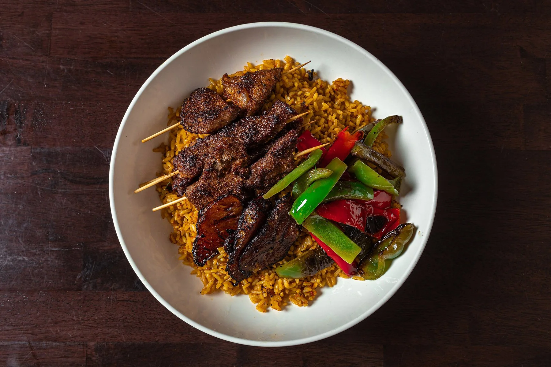 Grilled meat skewers with colorful roasted peppers served over seasoned yellow rice