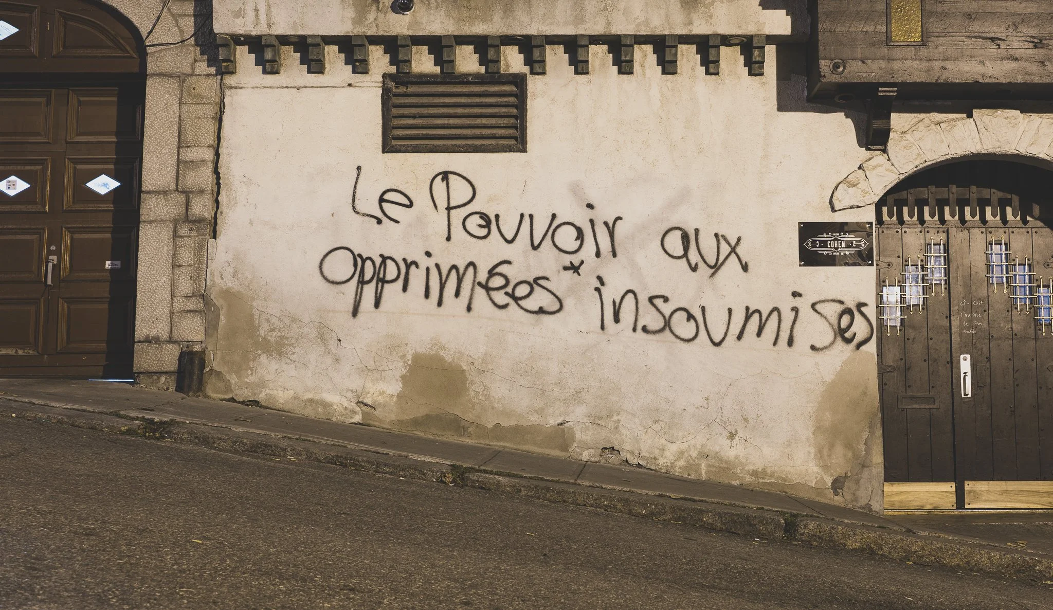 Graffiti sur un mur en pierre d'une phrase en français : « Le Pouvoir aux opprimés insoumis ».