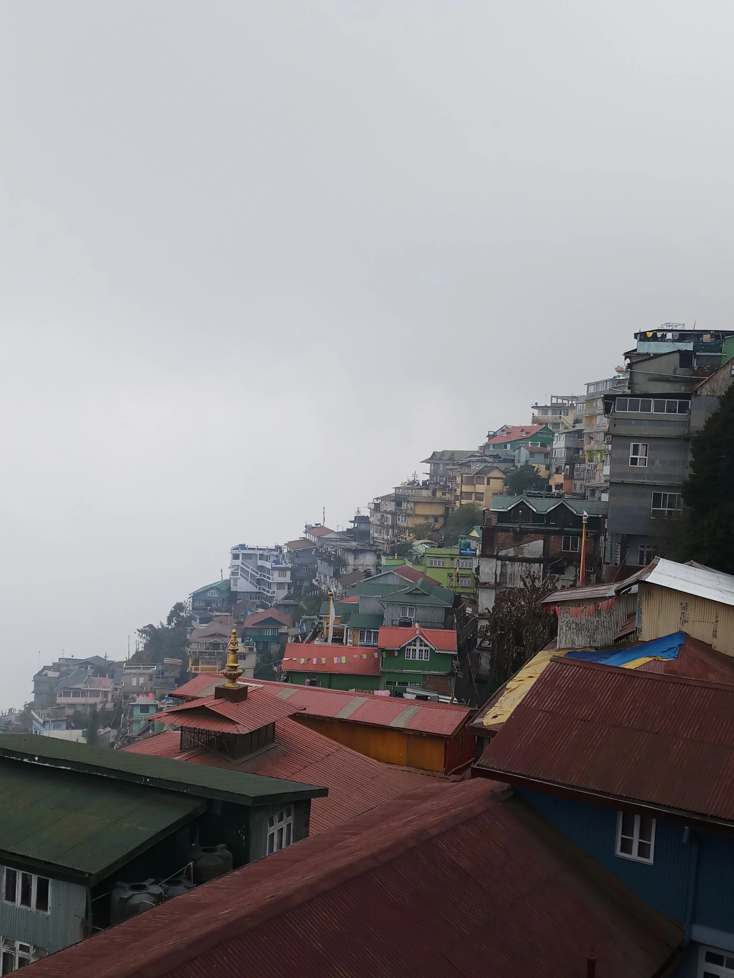 Vue de maisons colorées perchées sur une colline, avec un ciel nuageux en arrière-plan.