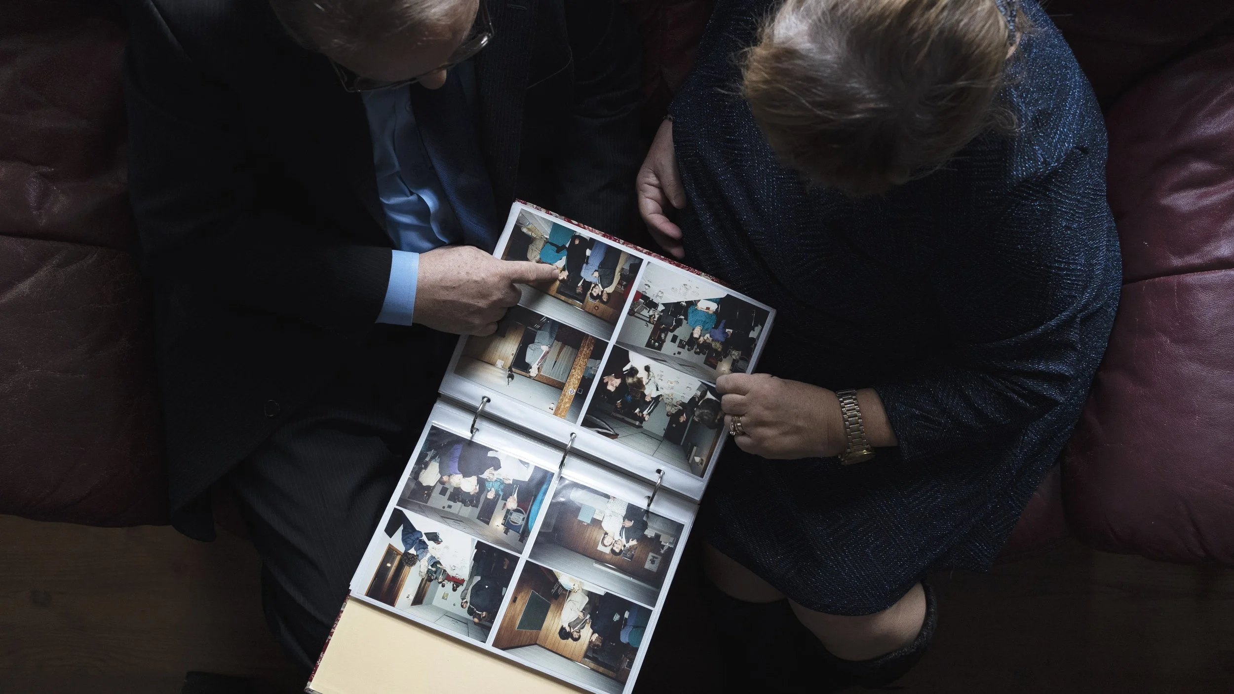 Deux personnes regardent un album photo avec plusieurs images imprimées, assises sur un canapé en cuir rouge.