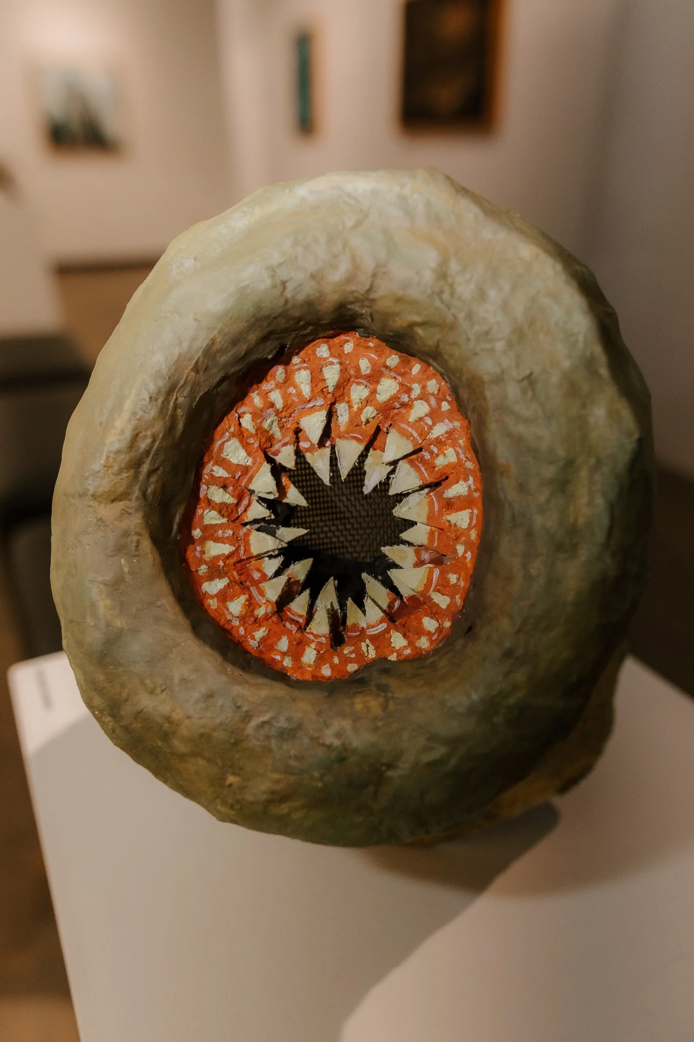 An abstract sculpture resembling an eyeball with a textured outer surface and a circular inner design with orange, black, and white details.