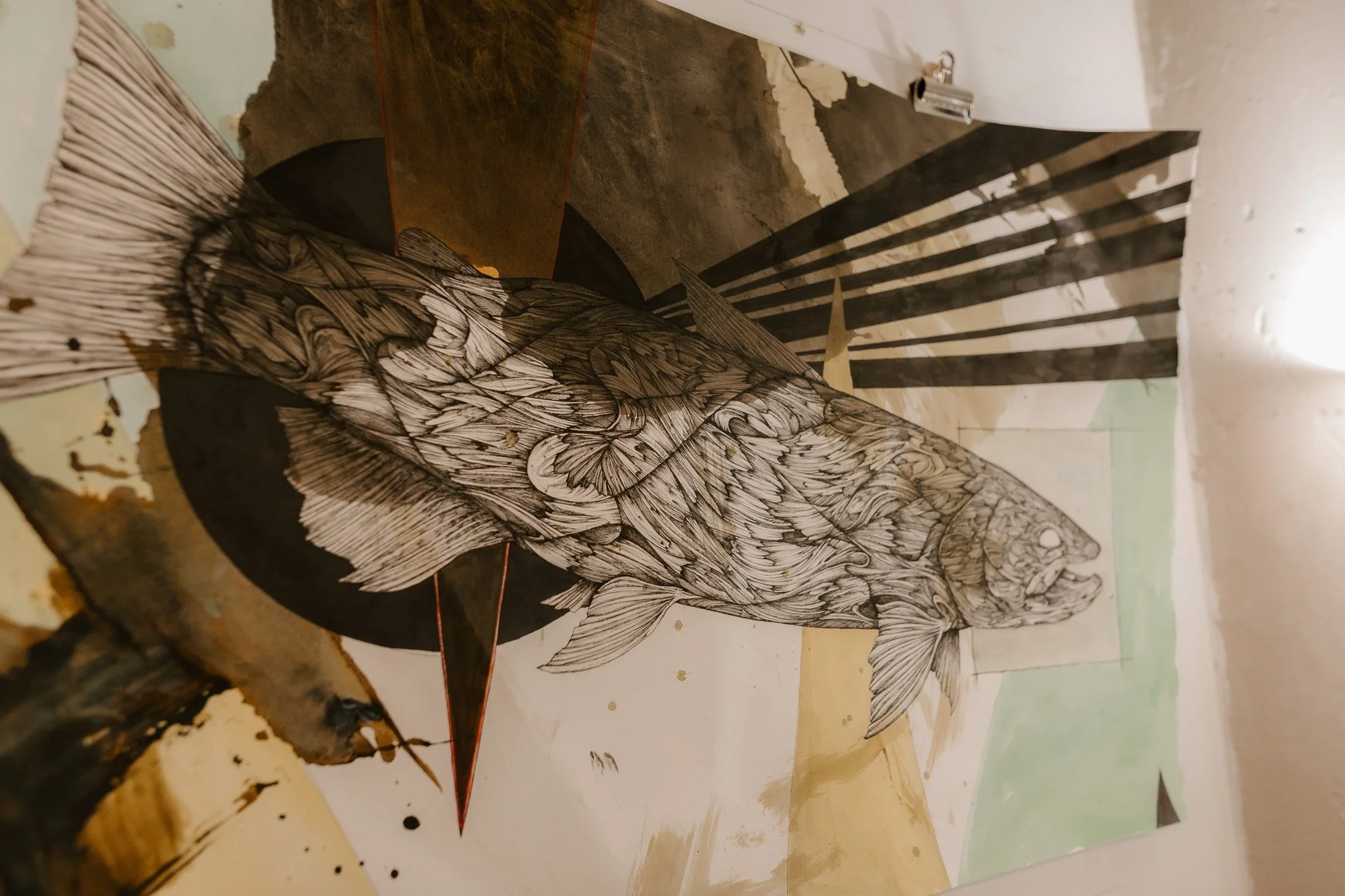 A detailed black and white drawing of a fish with intricate scales and fins, placed on top of a map.