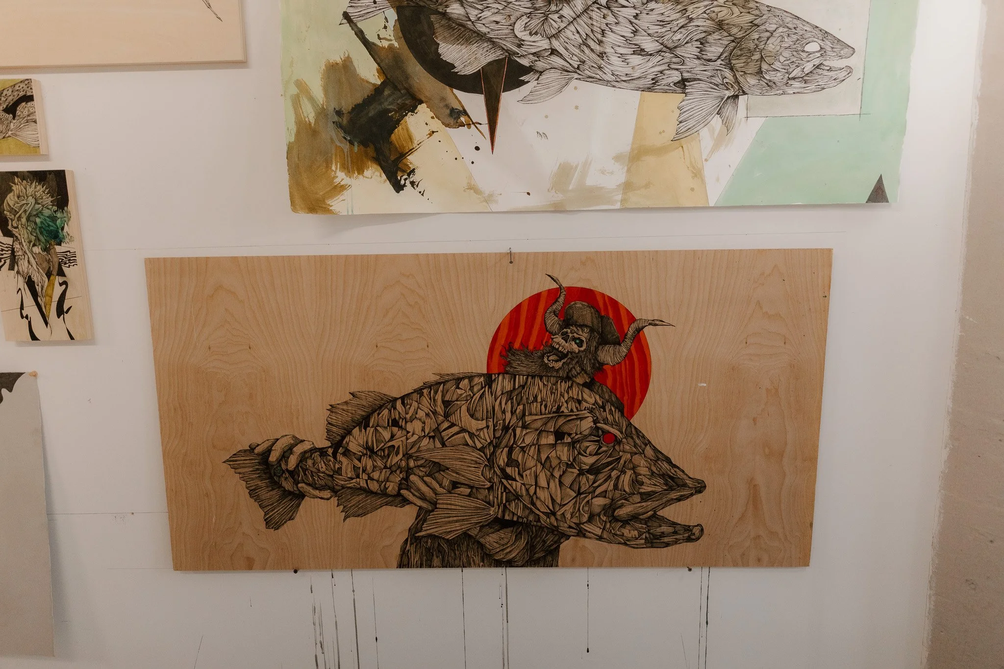 Artwork featuring a large fish with geometric details, a red sun behind it, and a creature with horns and a bearded face riding on the fish.