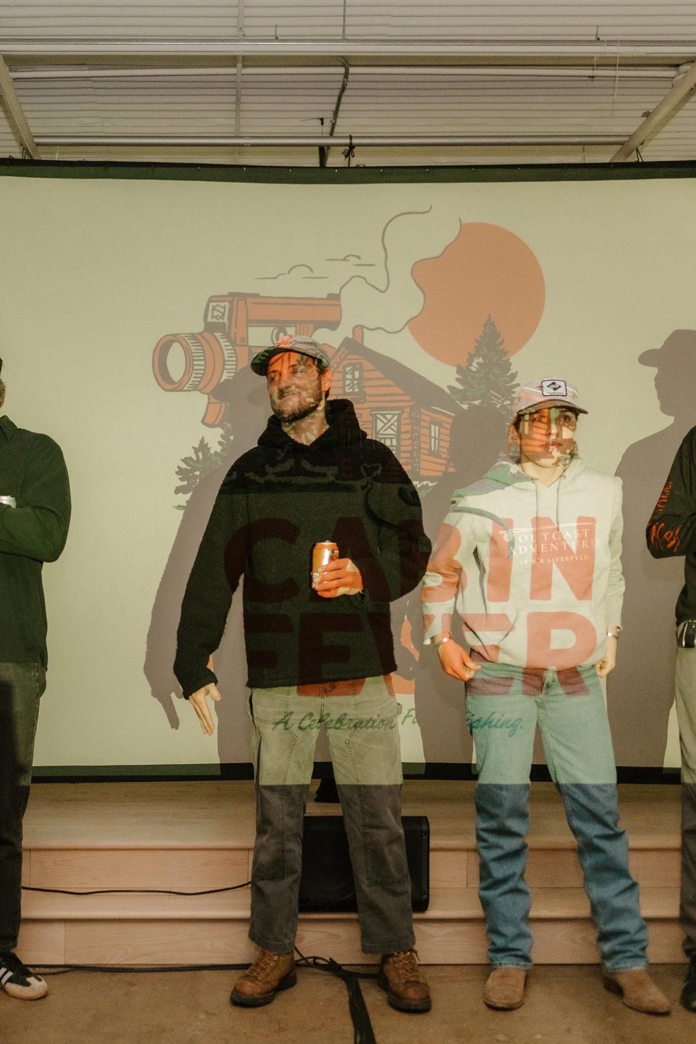 People standing on a stage with a projected background of a mountain cabin, trees, and a sun, with shadows cast on the screen.