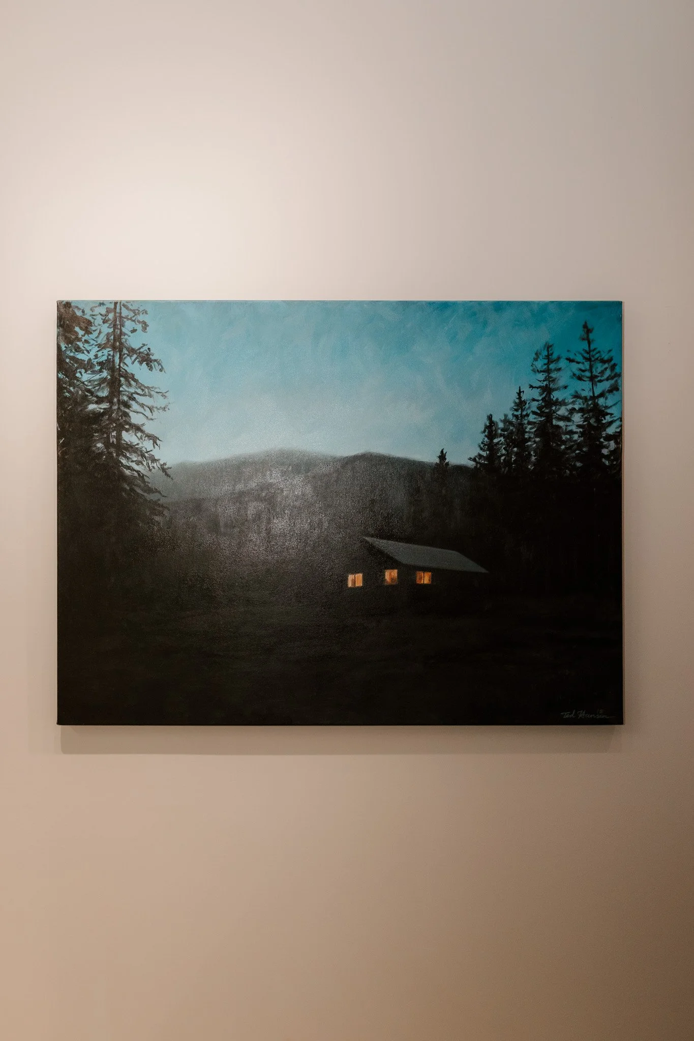 A painting of a dark forest landscape at dusk with a small house with lit windows, trees, mountains, and a blue sky.