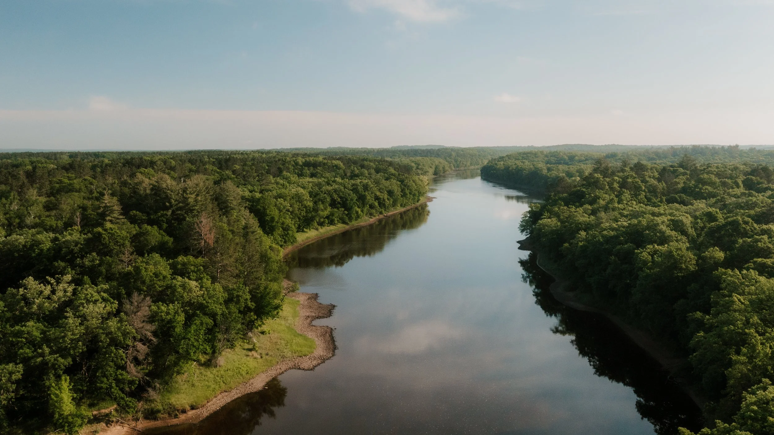 Aerial view of a winding river through a lush green forest under a partly cloudy sky.