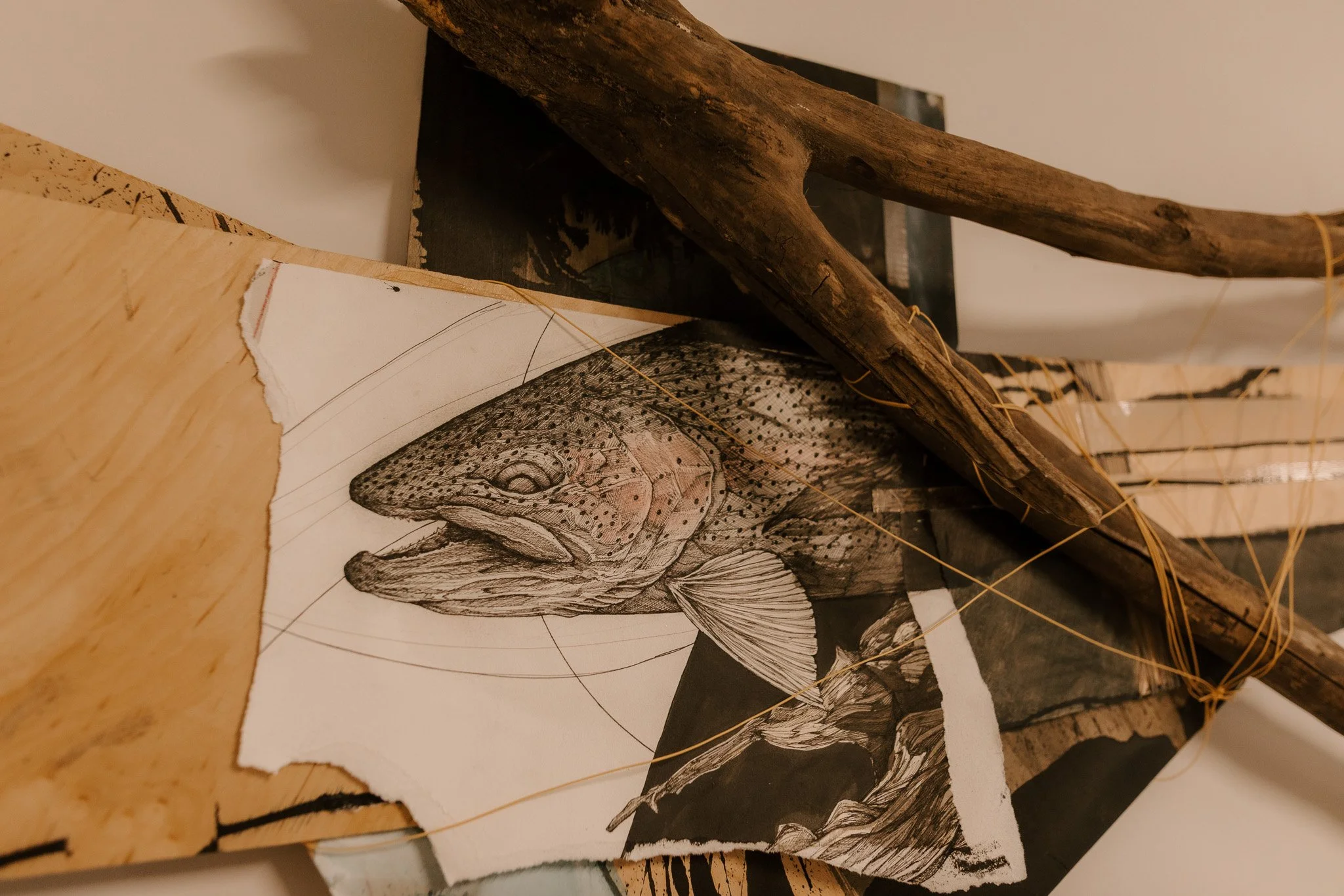 An art piece featuring a detailed black and white drawing of a fish, surrounded by wooden and textured black materials, with yellow string decoration.