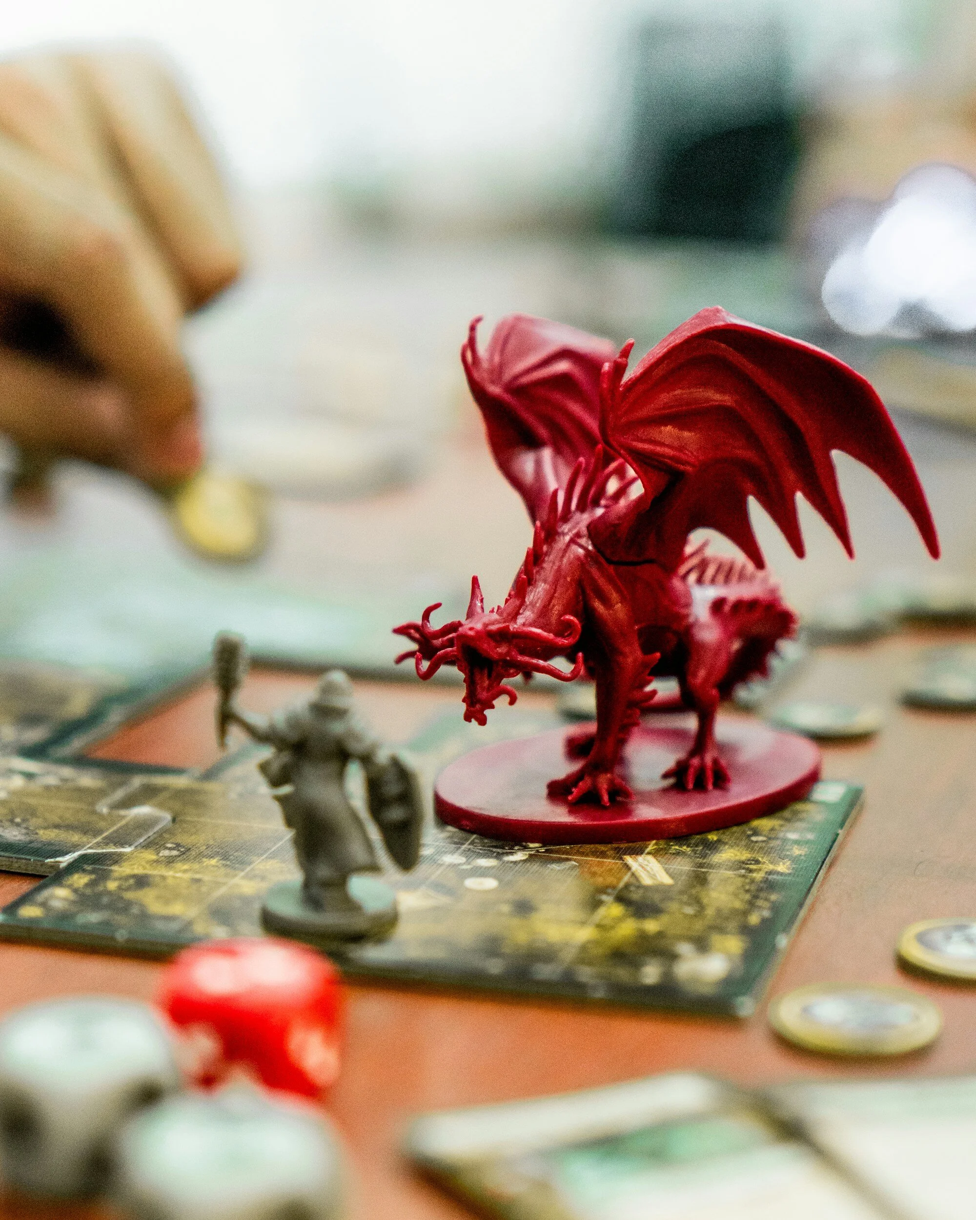 Red dragon figurine on a board game table surrounded by game pieces and cards.
