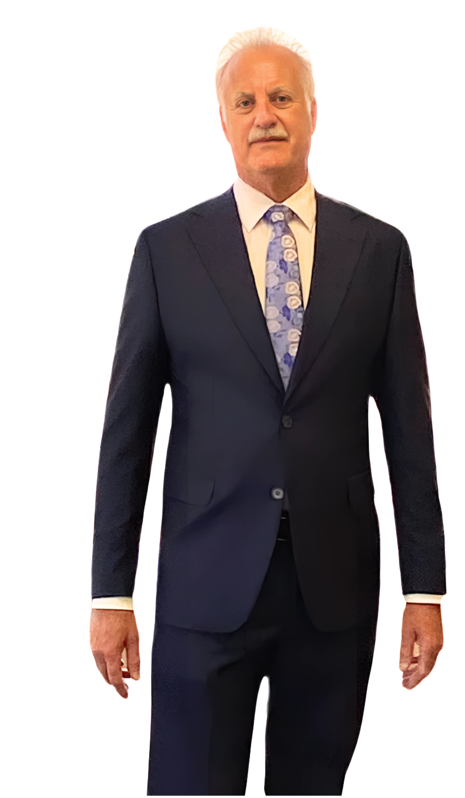 An older man with white hair and a mustache wearing a black suit, white shirt, and a floral tie, standing against a white background.