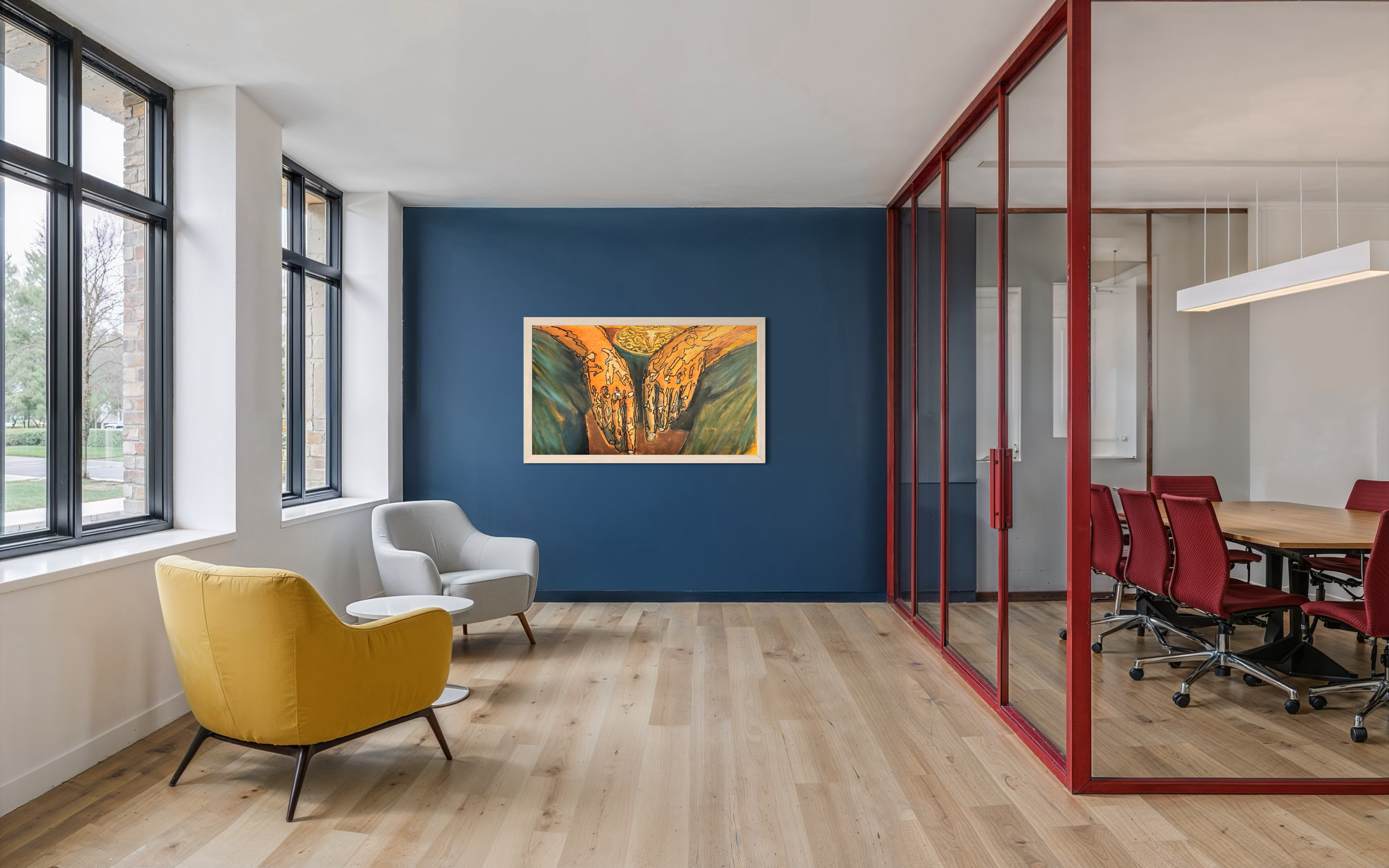 Modern office space with large windows, a blue accent wall with framed abstract art, white and yellow armchairs, and a conference room with red chairs enclosed in a glass wall.