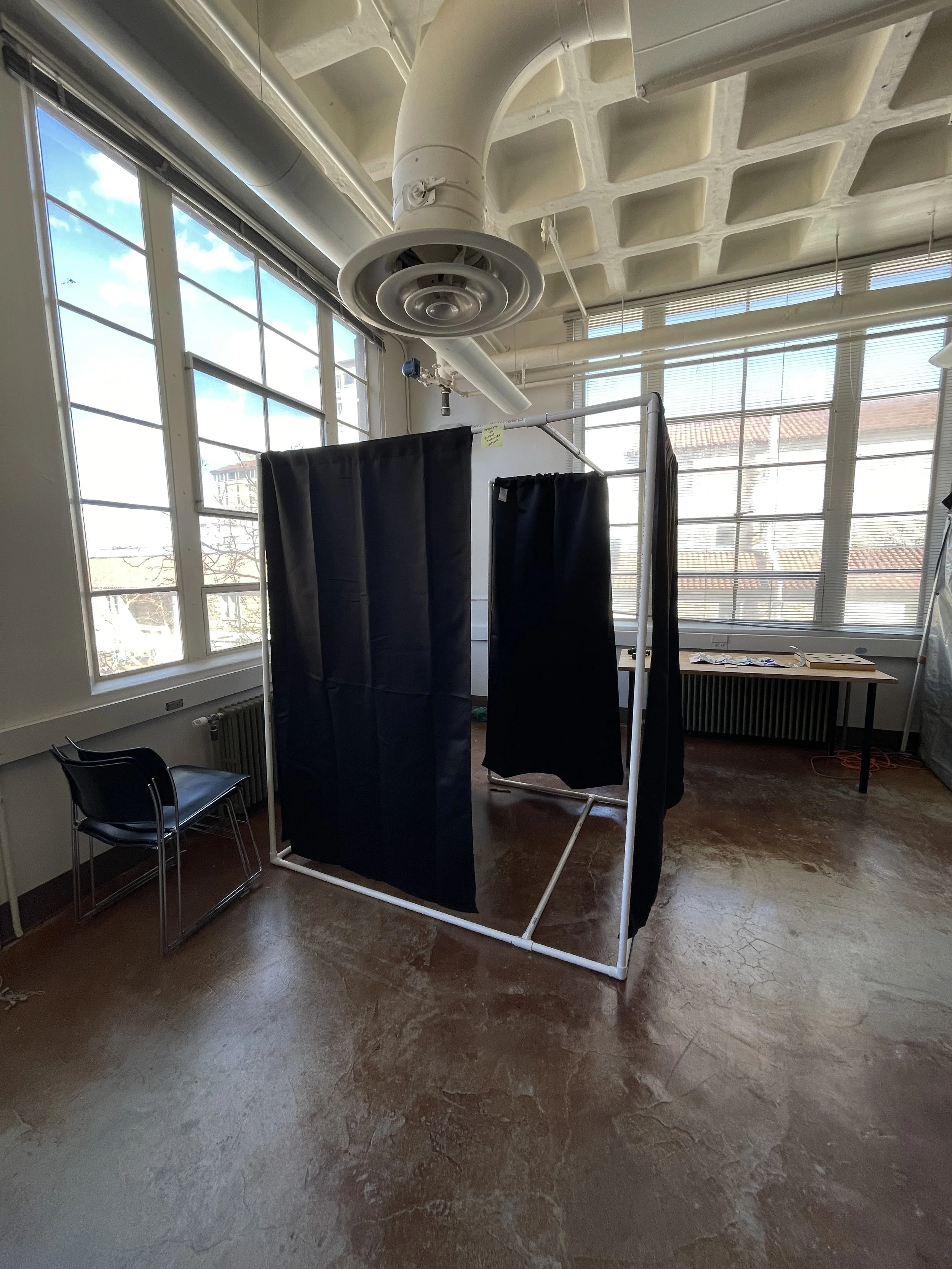 Room with a white frame structure and black curtains, large windows, and ceiling vents