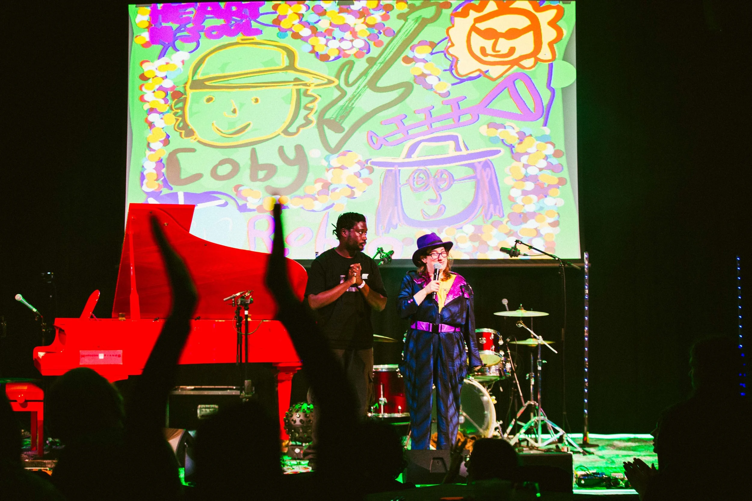 Robyn Rocket and Coby Sey on stage witha. red piano and drum kit , behind them is a hand drawn projected picture of them . photo by Sian O Connor 