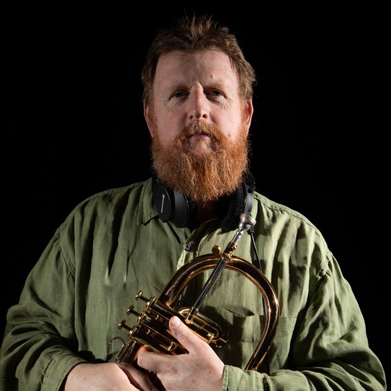 Photo Duncan chapman - a white man with red beard and short hair in a green shirt holding a flugalhorn