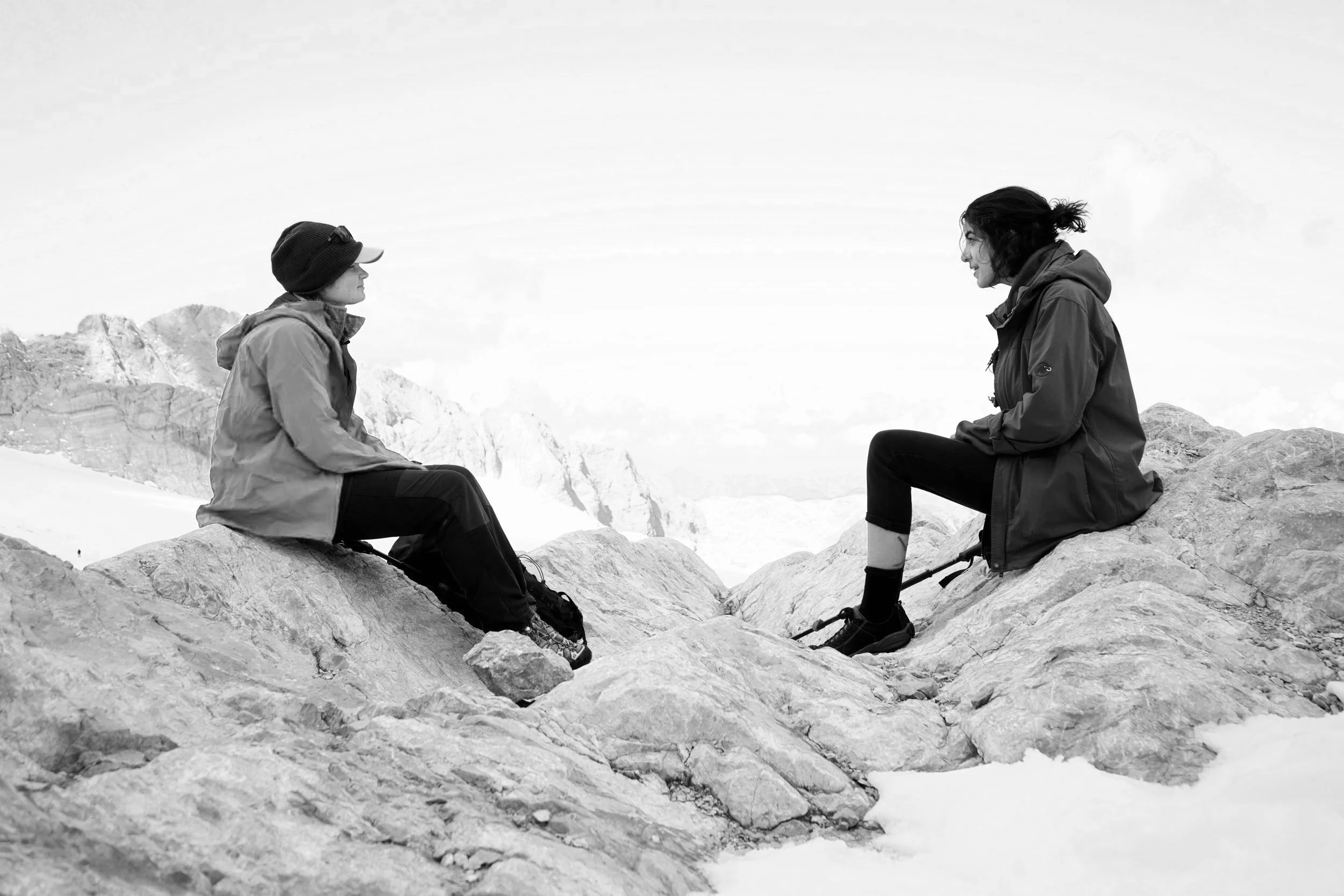 Sarah und Glaziologin Lea Hartl sitzen einander gegenüber auf Felsen, die von Schnee umgeben sind