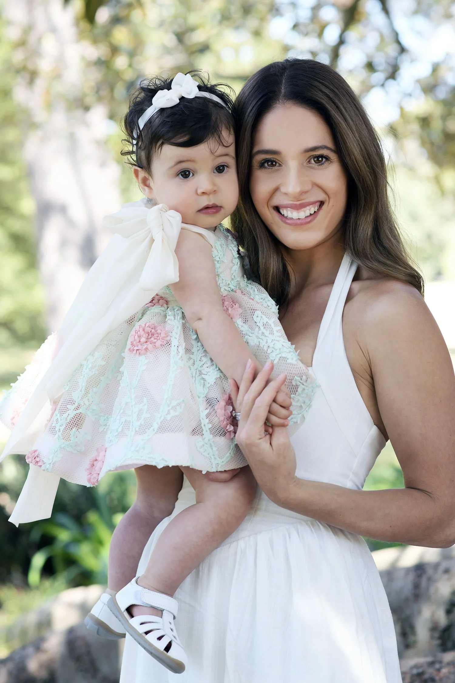 Portrait of pretty mother in white with young baby in a park 
