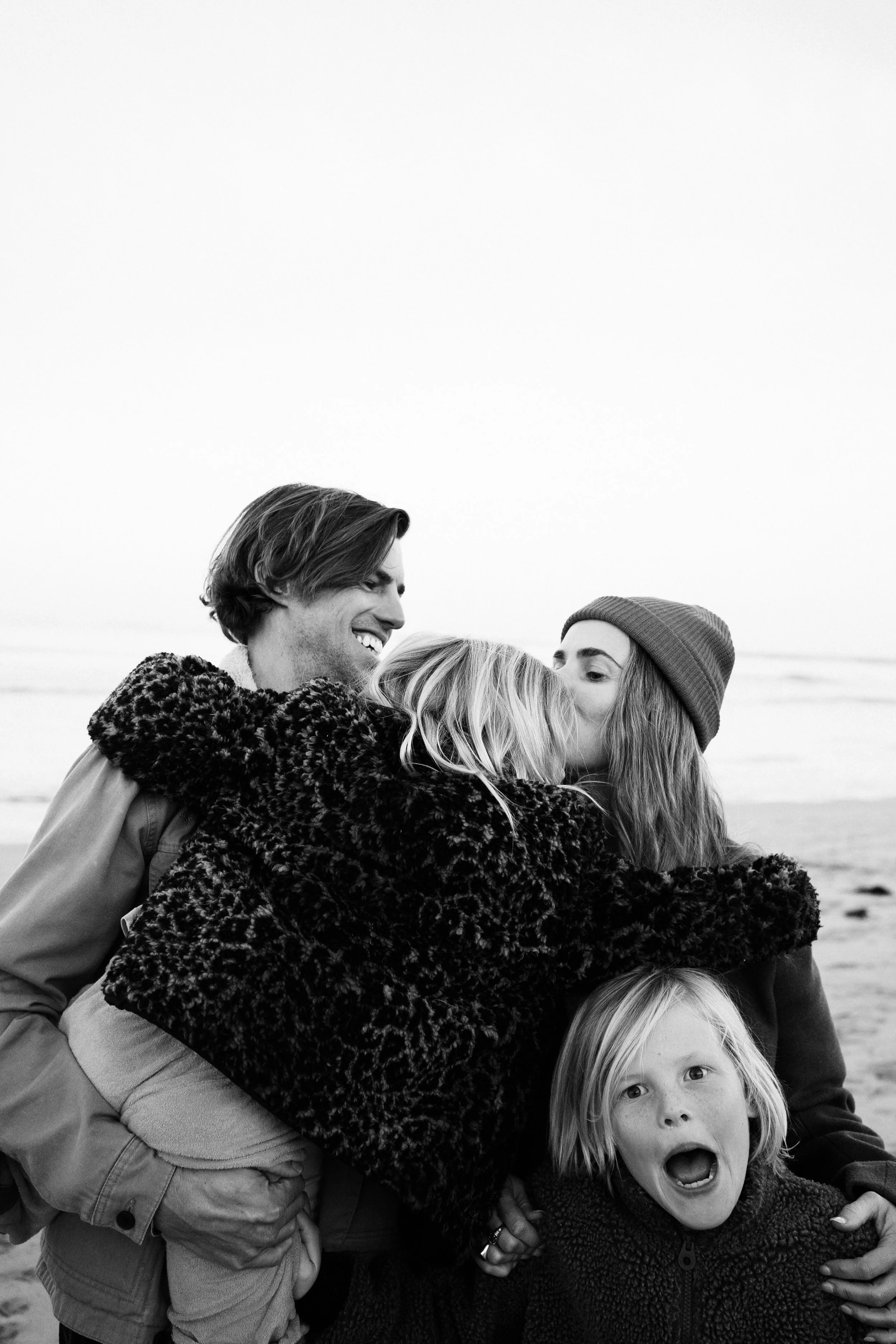 A group of children and a young man sharing a hug outdoors, with the children showing surprised and joyful expressions.