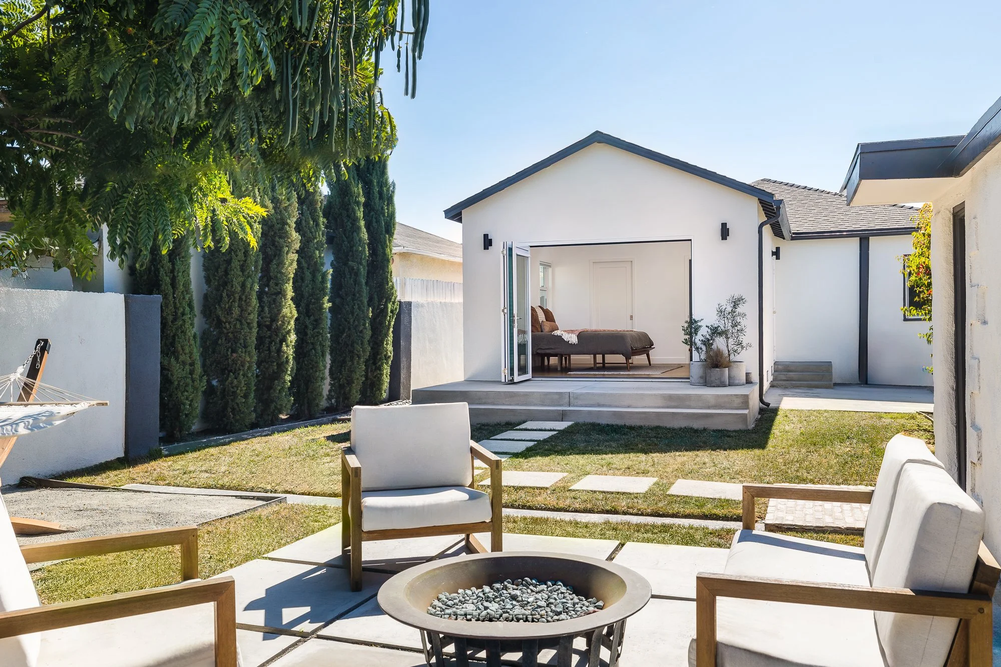 Landscaped backyard with fire pit seating area and detached room with open bi-fold doors in a South Bay home remodel