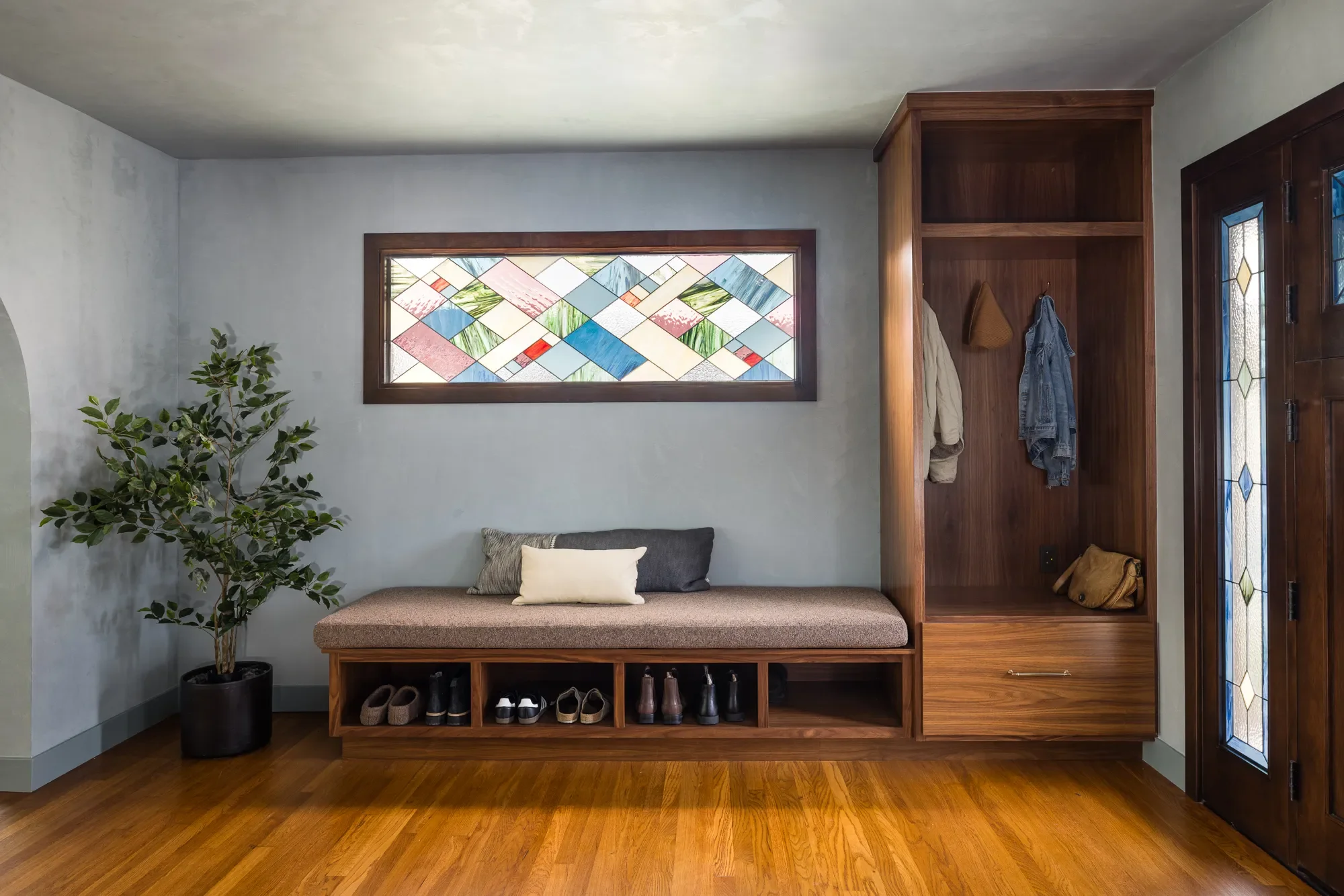 Built-in entryway bench with shoe storage and stained glass window in a Craftsman home