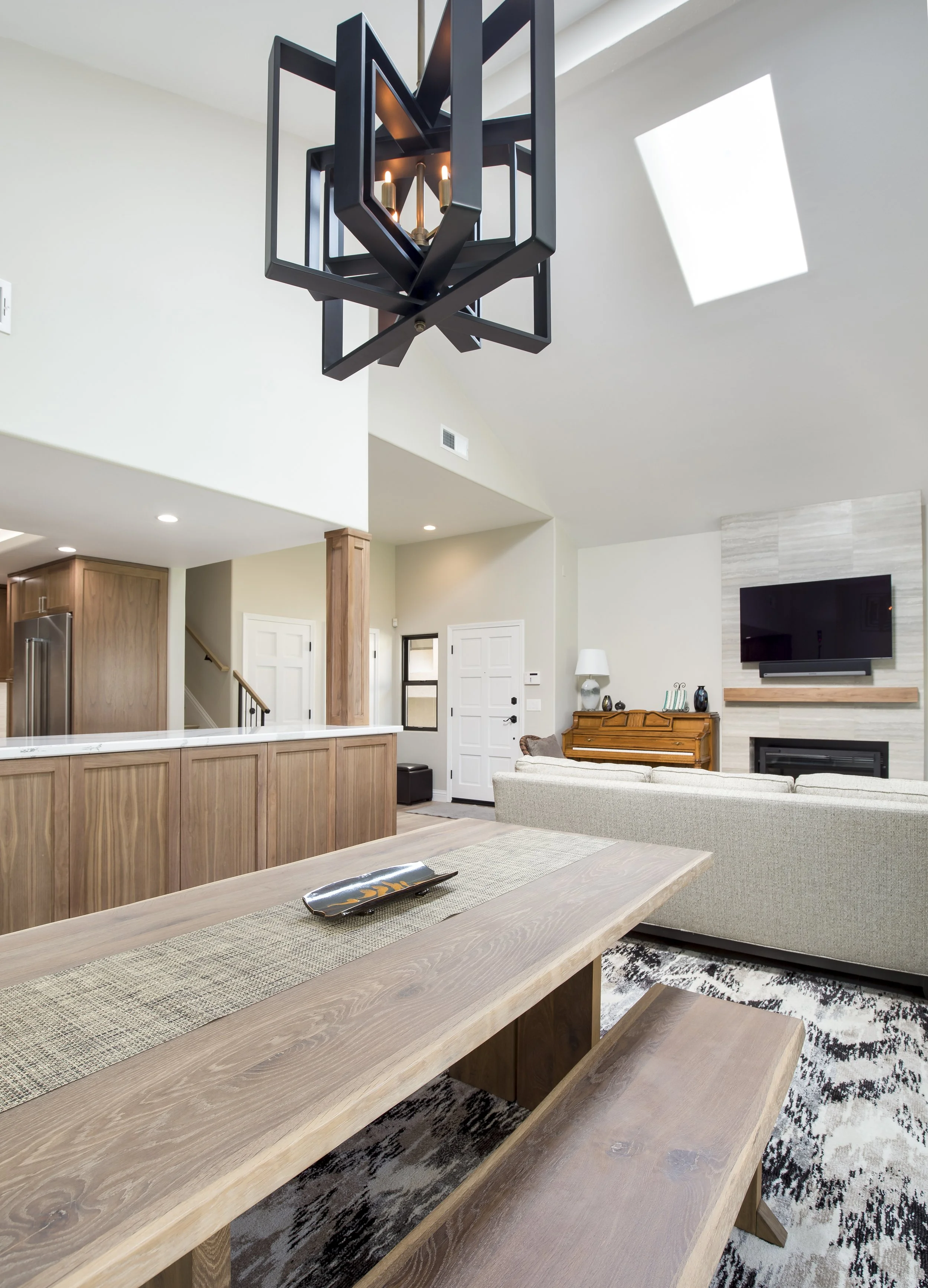 Open living space with a vaulted ceiling and skylight over a wooden dining table and bench