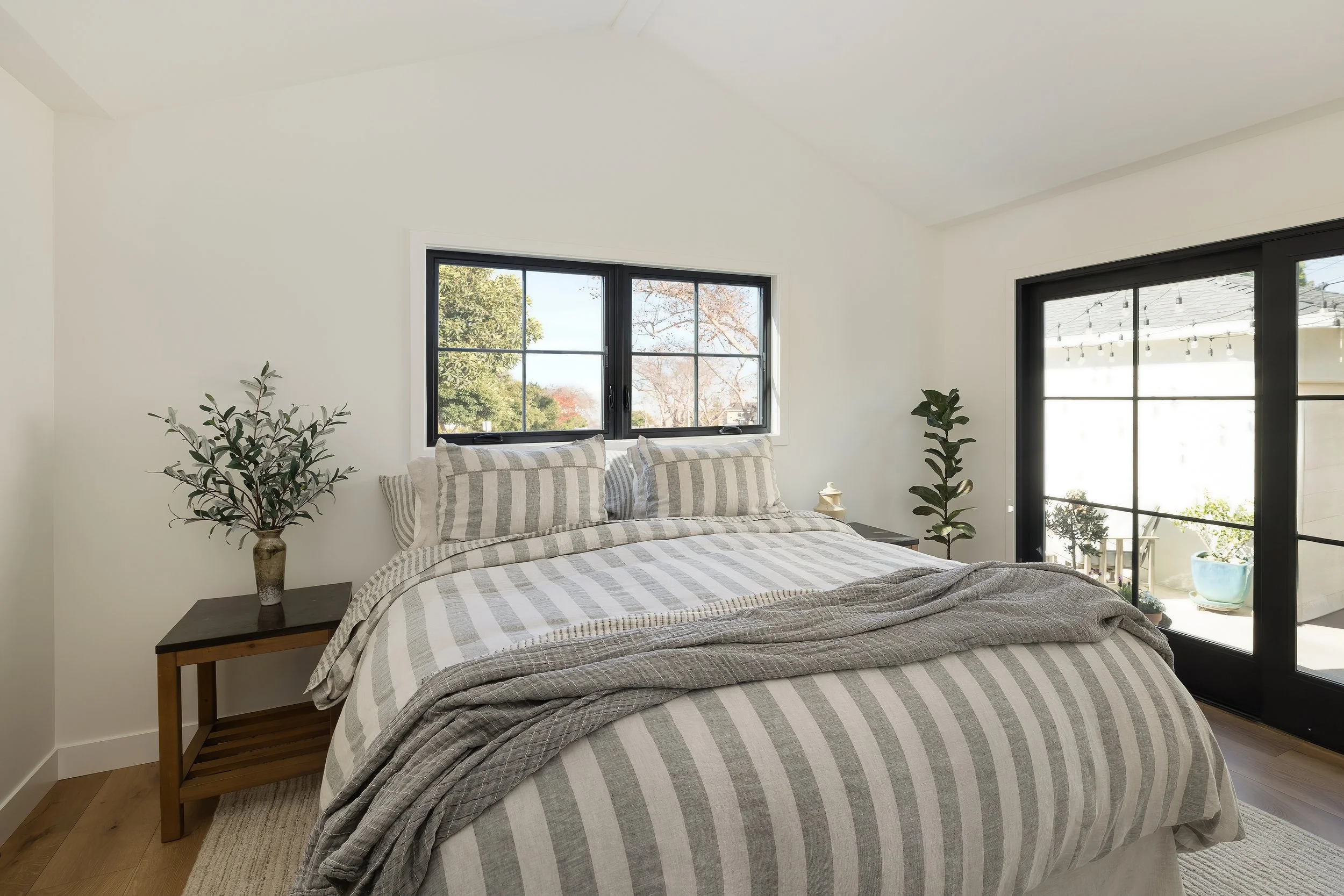 Bedroom with a vaulted white ceiling and black-framed windows above a bed with grey striped linens