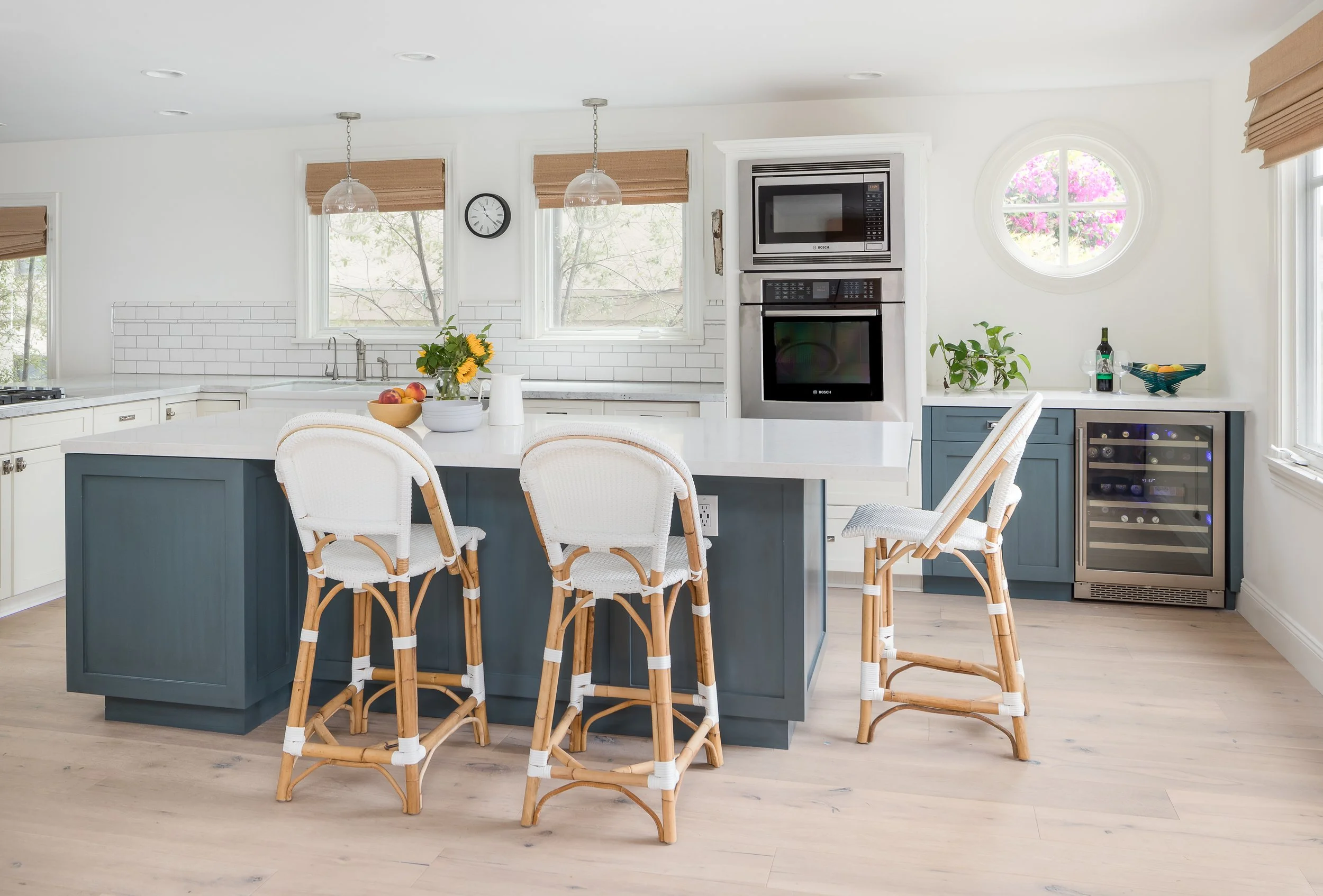 Bright white kitchen with a slate blue island, white countertops and rattan counter stools